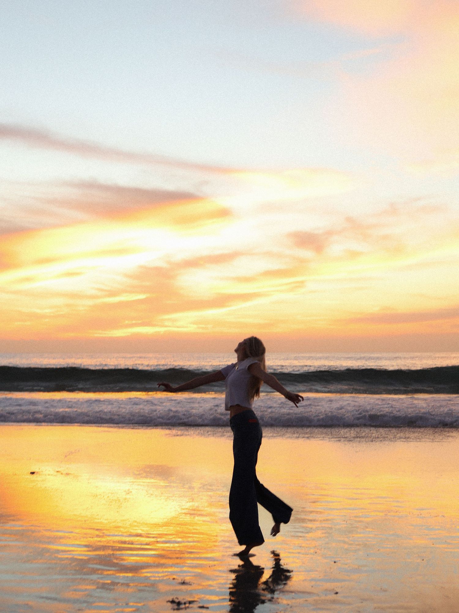 Silhouette of a person playing in shallow ocean water at sunset with vibrant orange and pink sky.