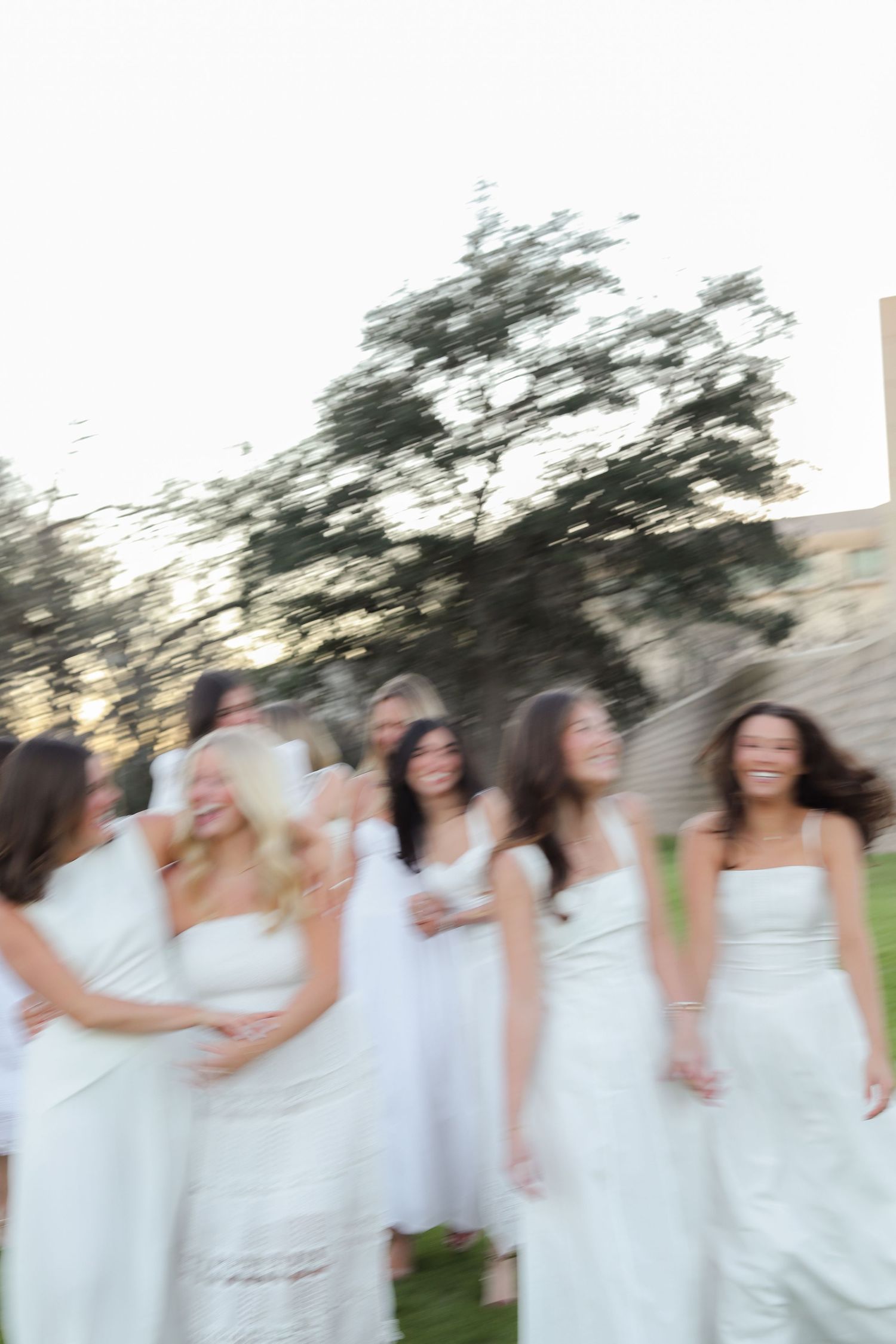 Motion-blurred photo of people in white dresses creating a joyful moment outdoors.