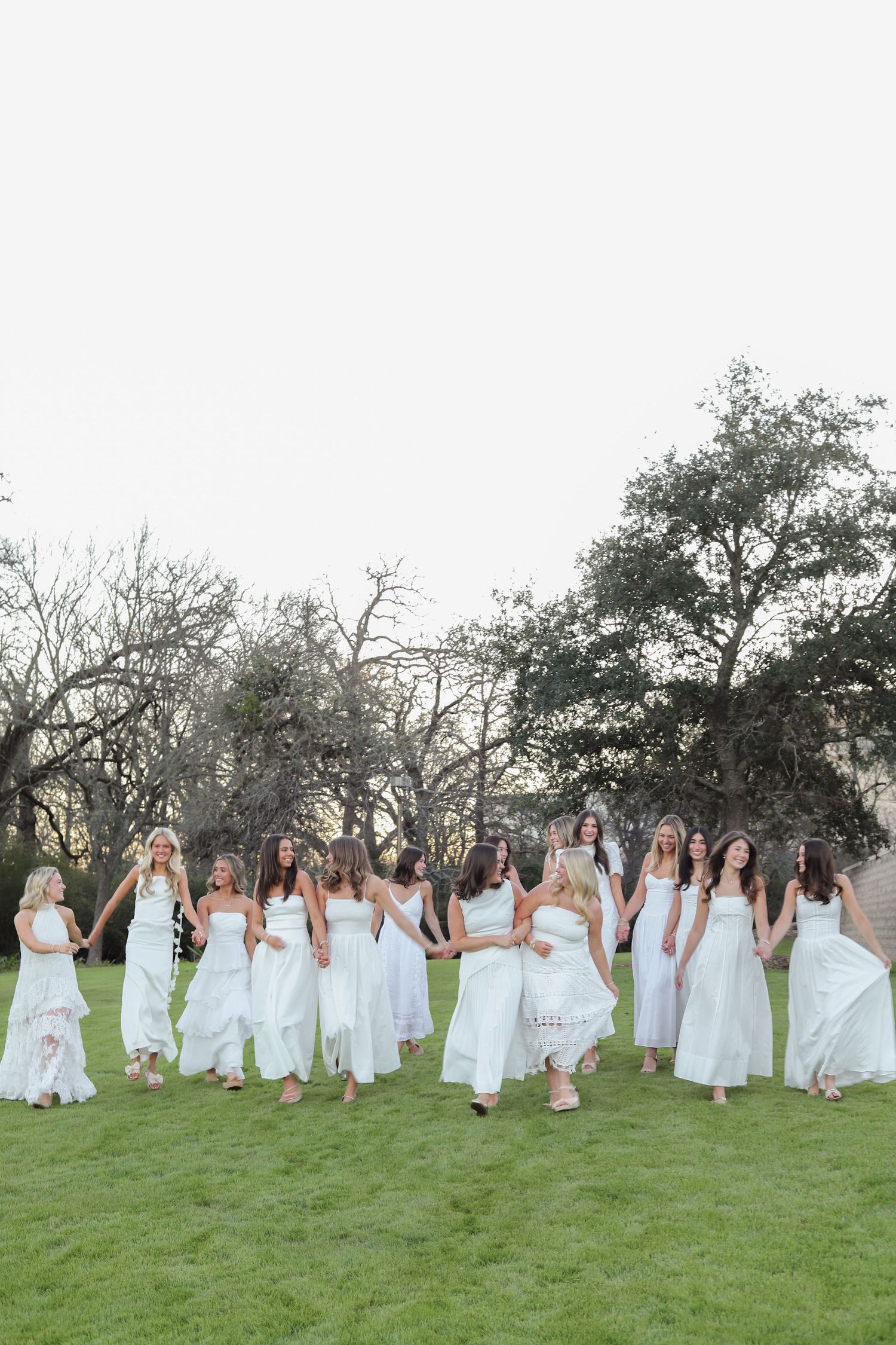 A festive group in white dresses spreads out across a hillside for a dynamic outdoor photo.
