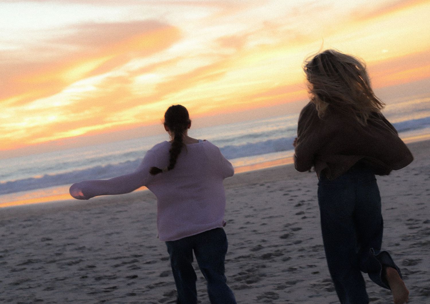 Silhouetted figures dance joyfully on a beach at sunset with vibrant orange and purple sky overhead.