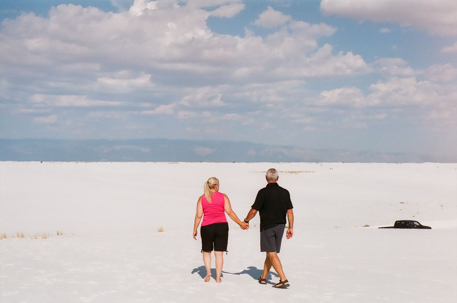 People walking along a pristine white sandy beach under a bright blue sky.