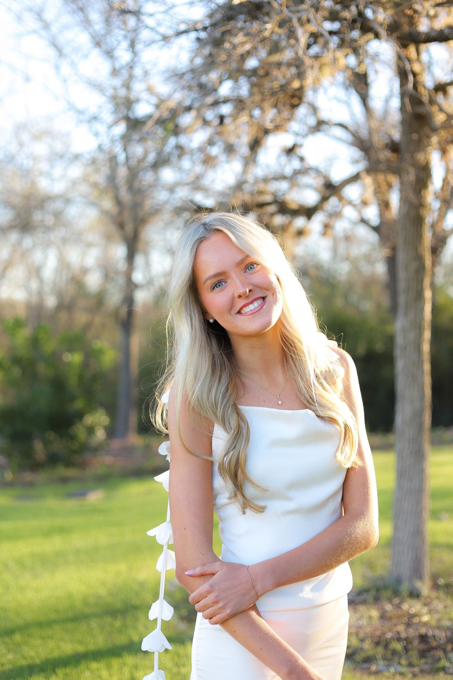 A sequence of playful poses in a white dress outdoors with trees and sunlit grass in the background.