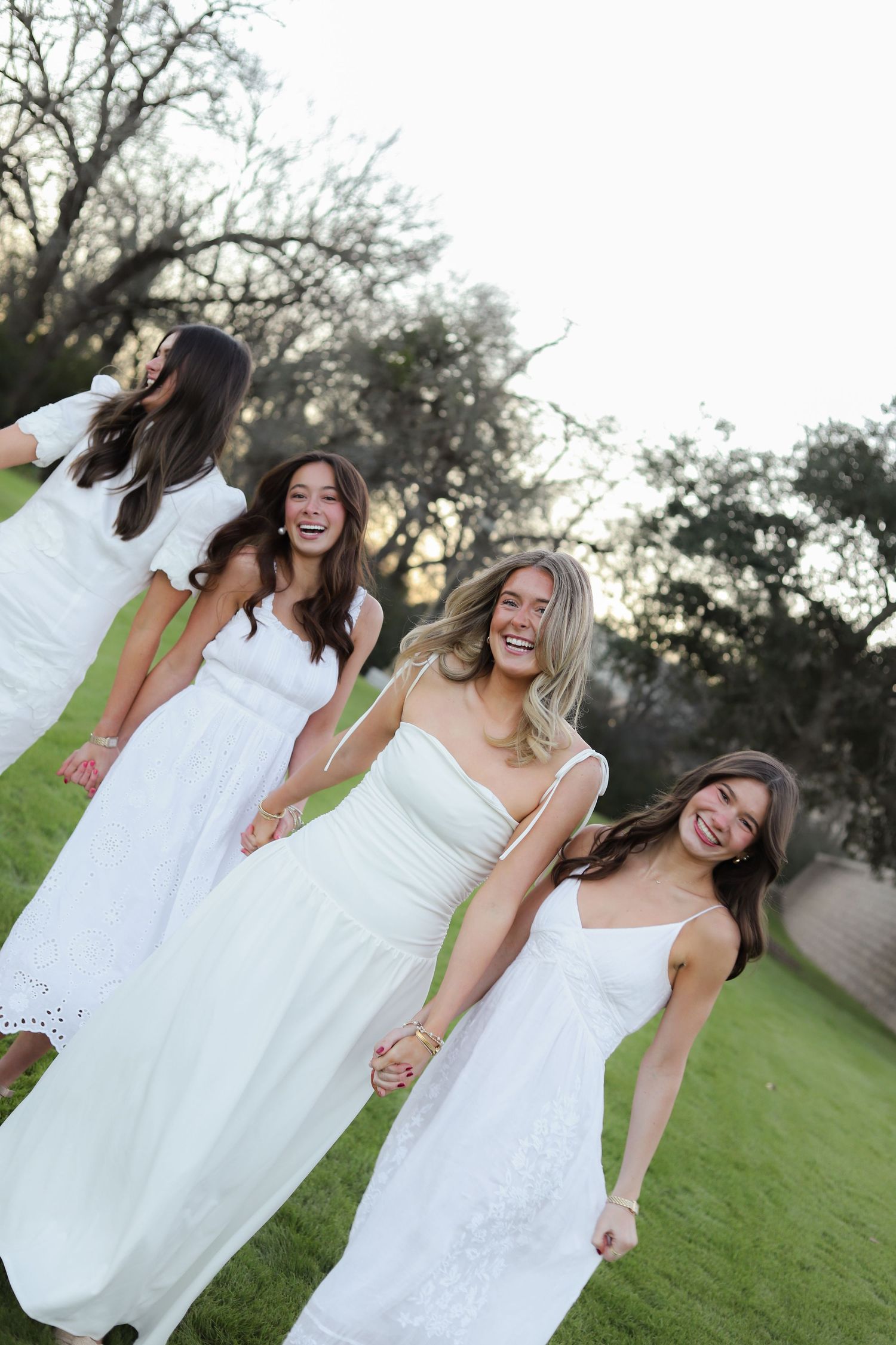 A group wearing matching white dresses laughs together during an outdoor photoshoot.
