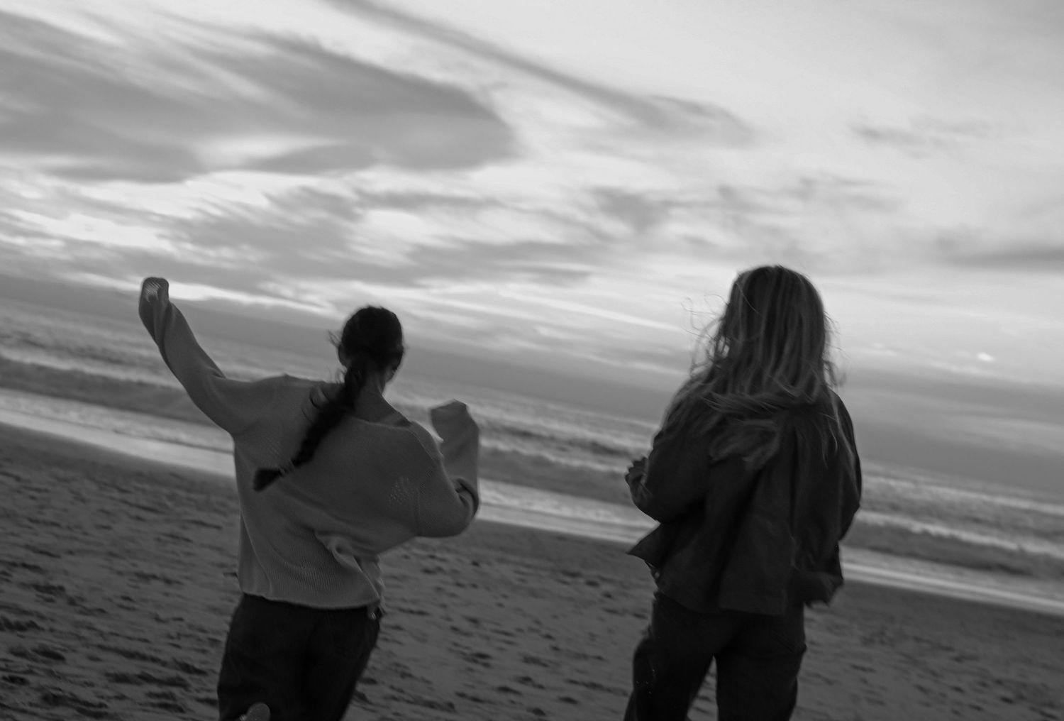 Silhouettes of people standing on a beach at sunset with dramatic cloudy skies in black and white photography.