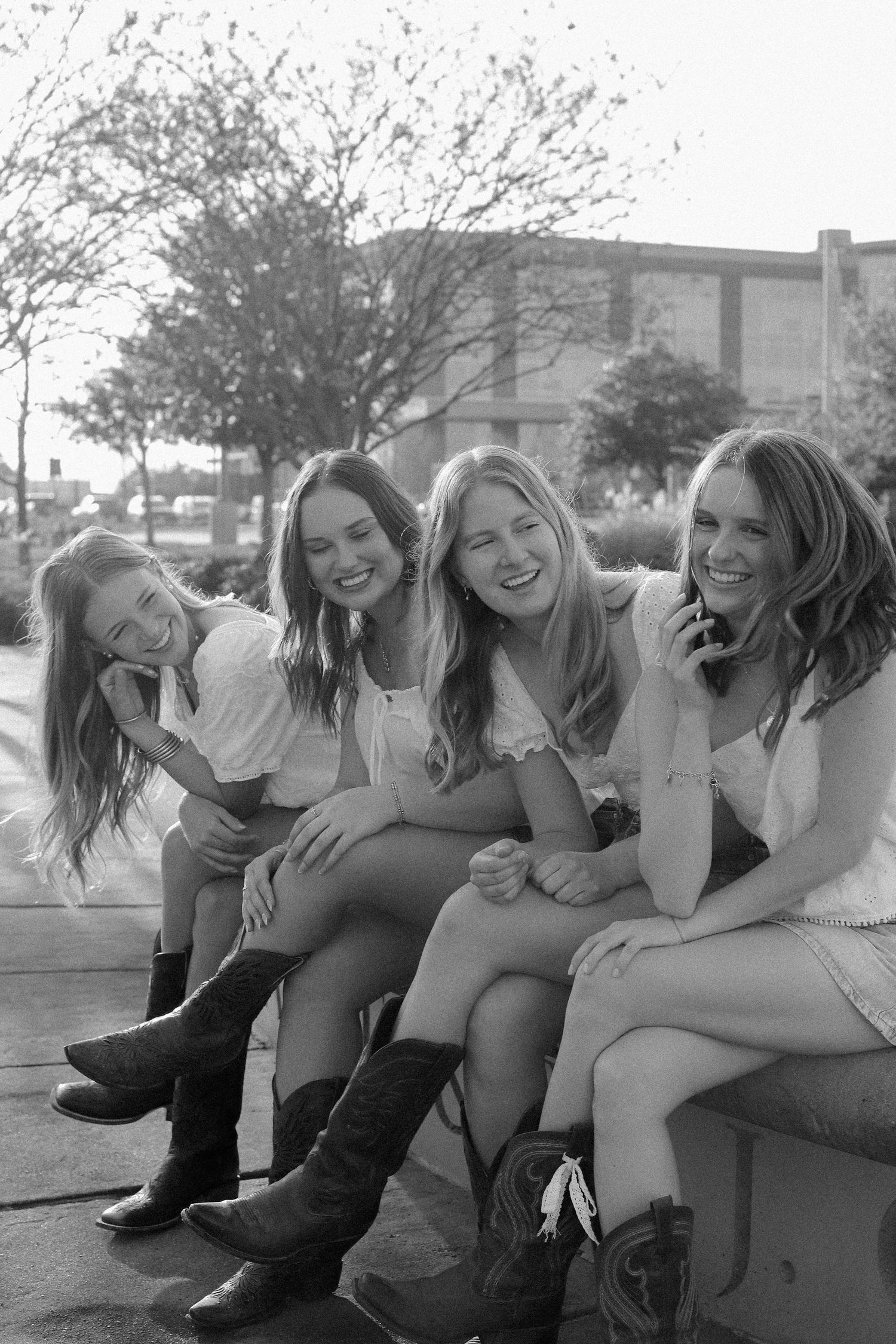 Group wearing boots and casual attire sit close together laughing outdoors in black and white.