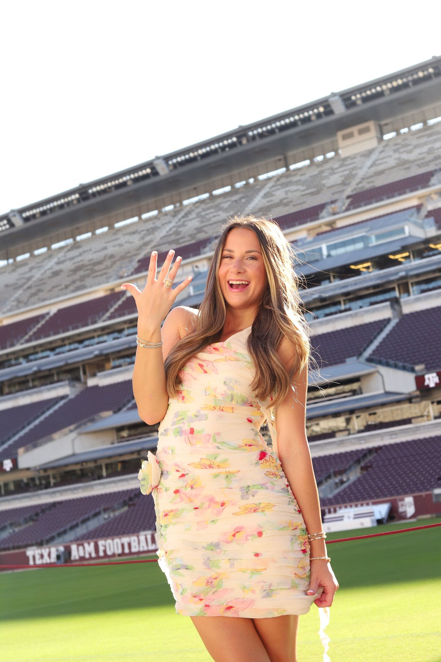 Dynamic poses in floral dress on football field with stadium seating in background.