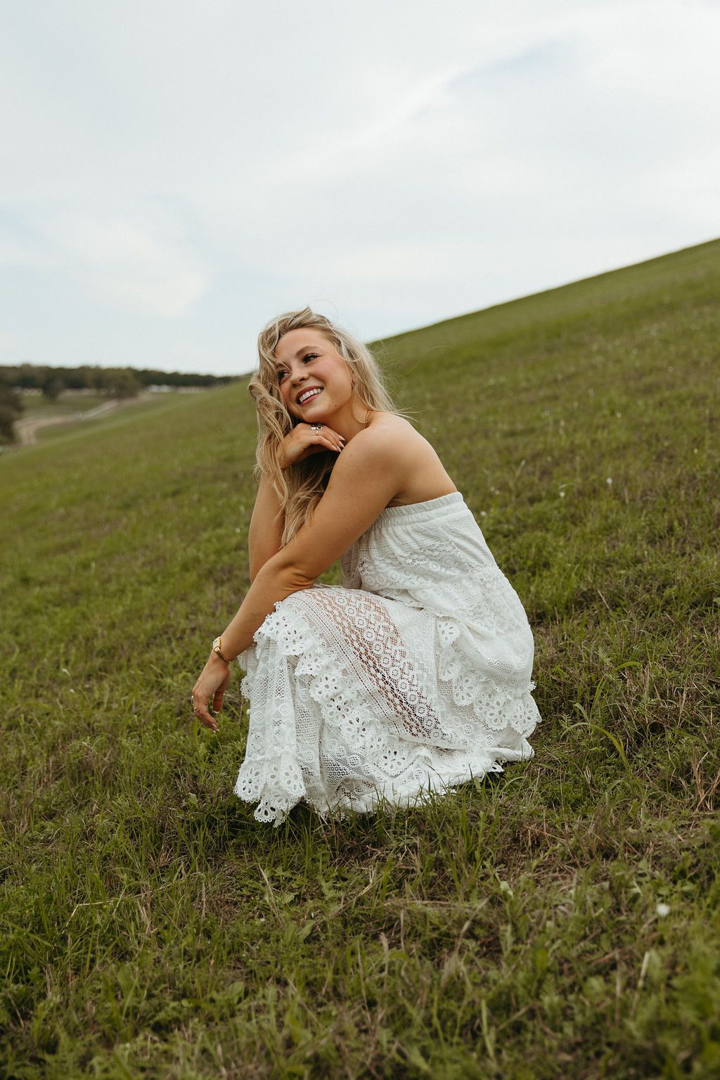 A white lace dress contrasts beautifully against a green hillside on a cloudy day.