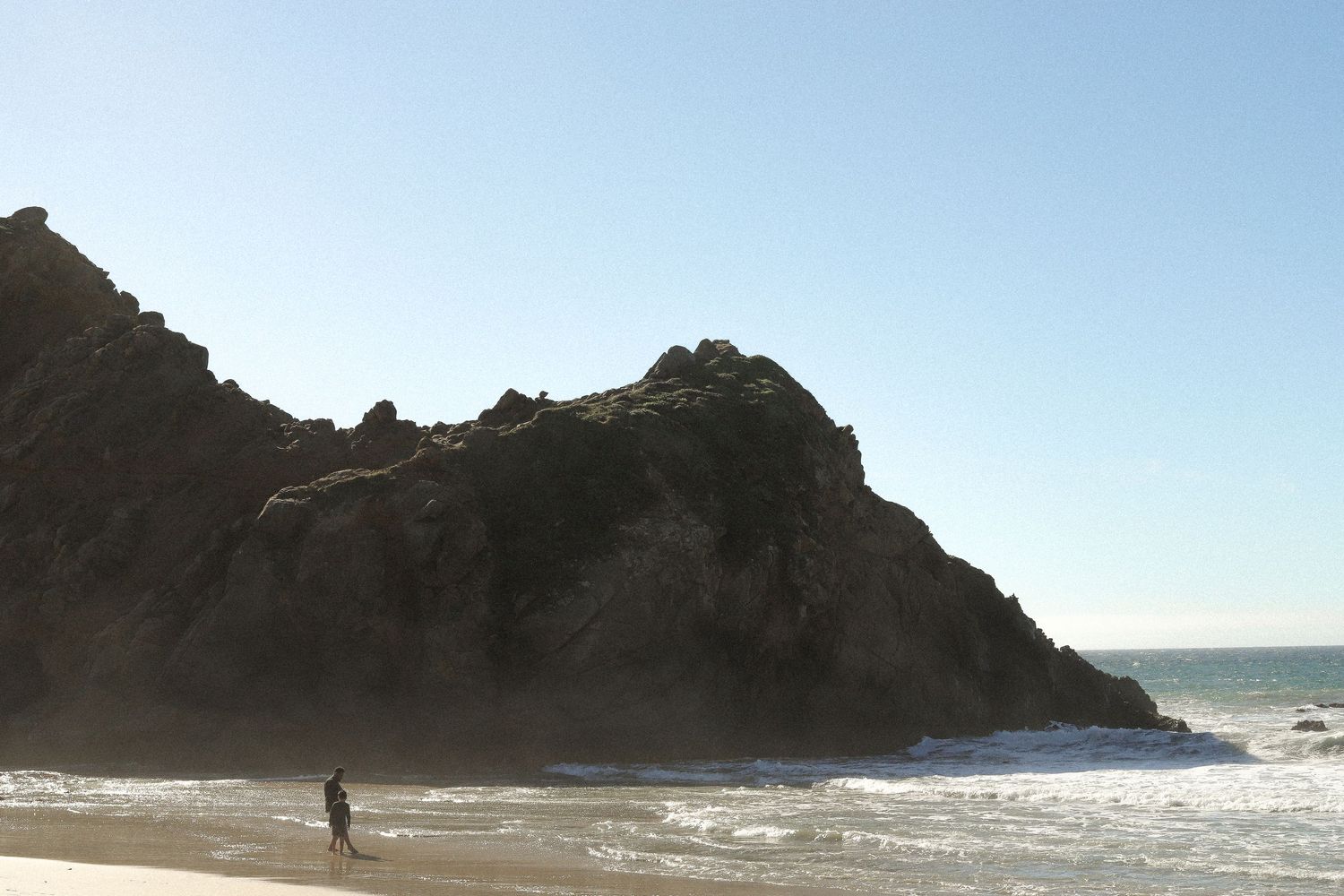 Rocky beach cove with dark cliffs and breaking waves along the shoreline.