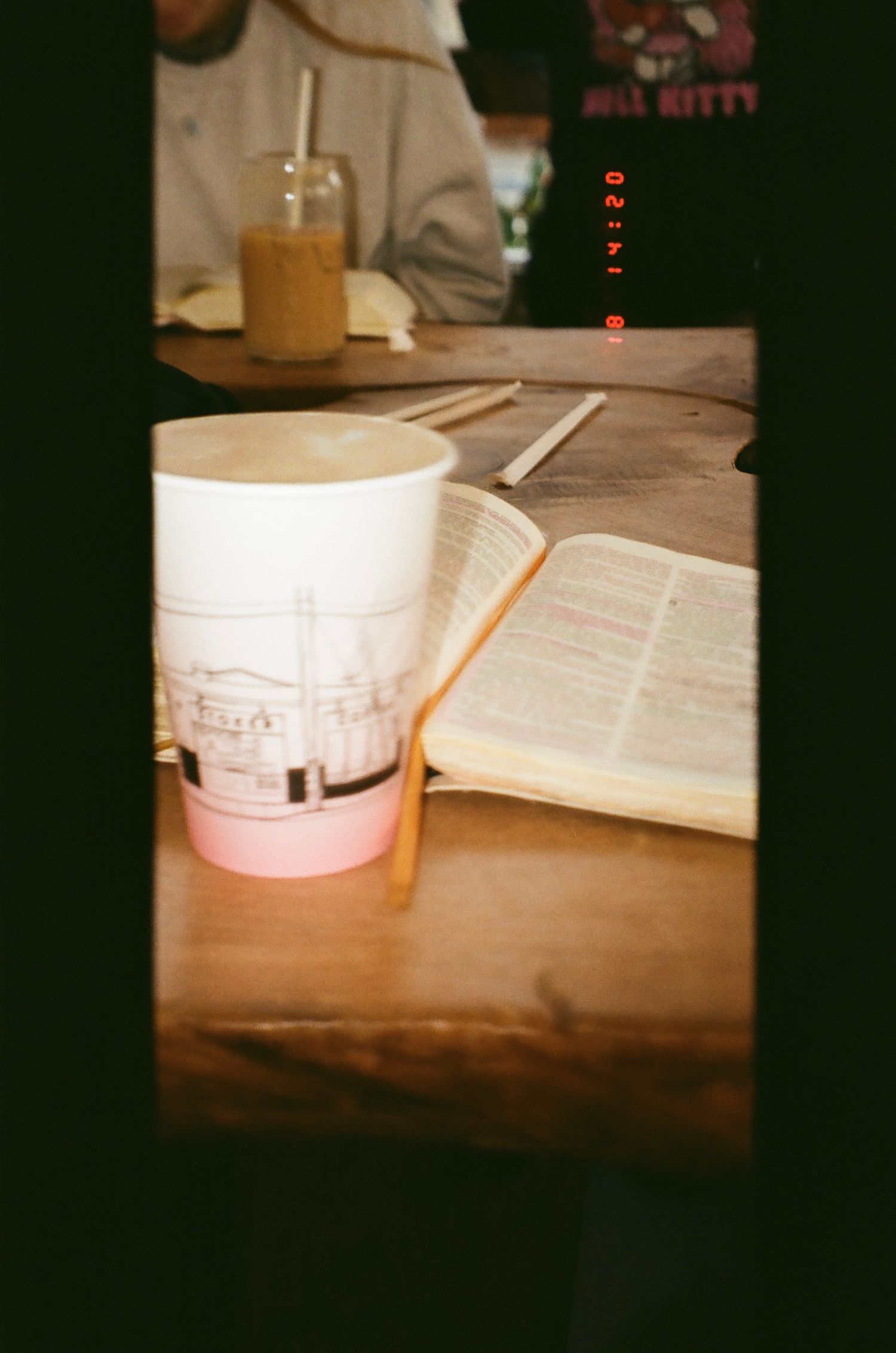 Study materials and textbooks laid out on a wooden desk with disposable coffee cups in dim lighting.