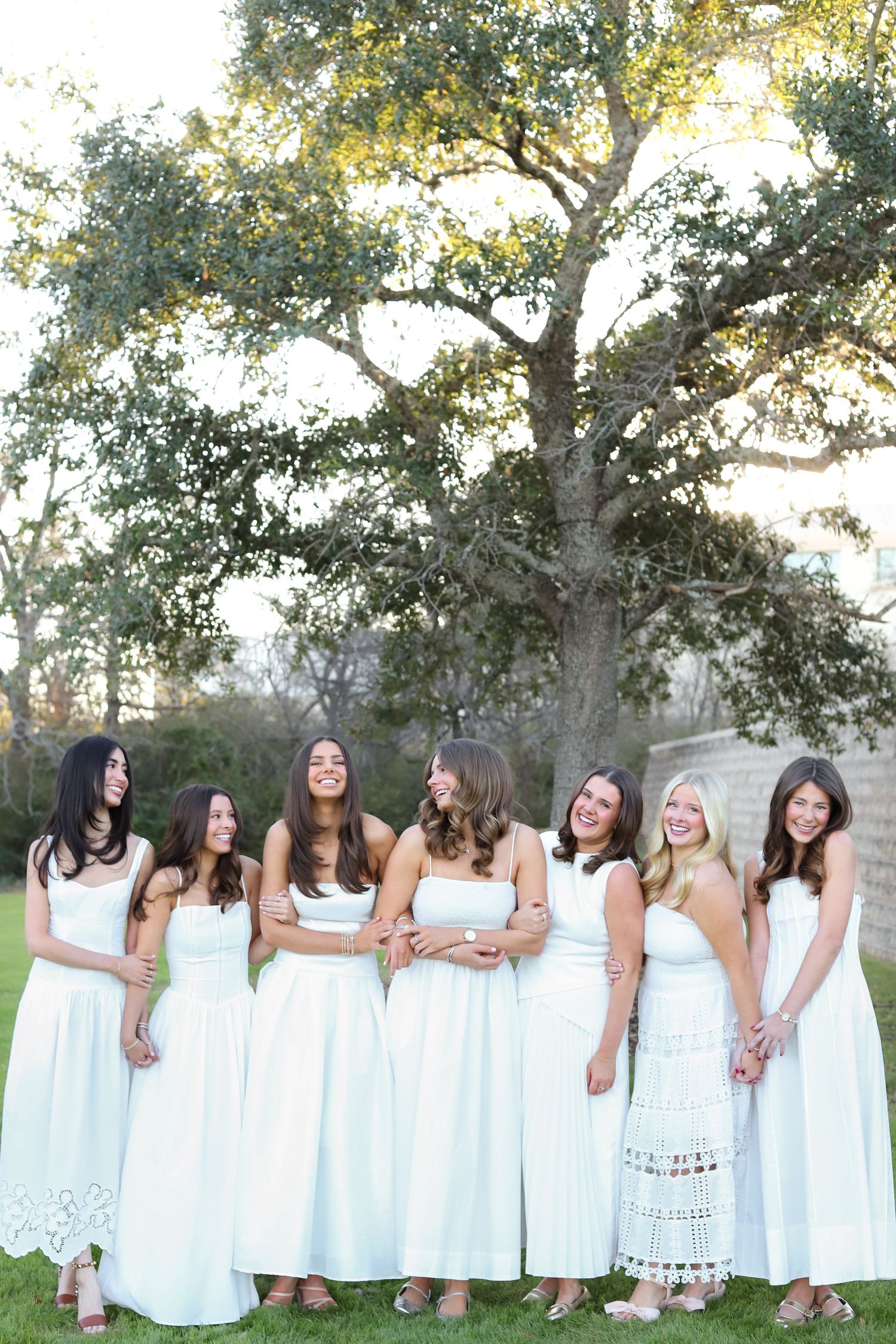 Group photo sequence showing women in white dresses posing together in a line outdoors.