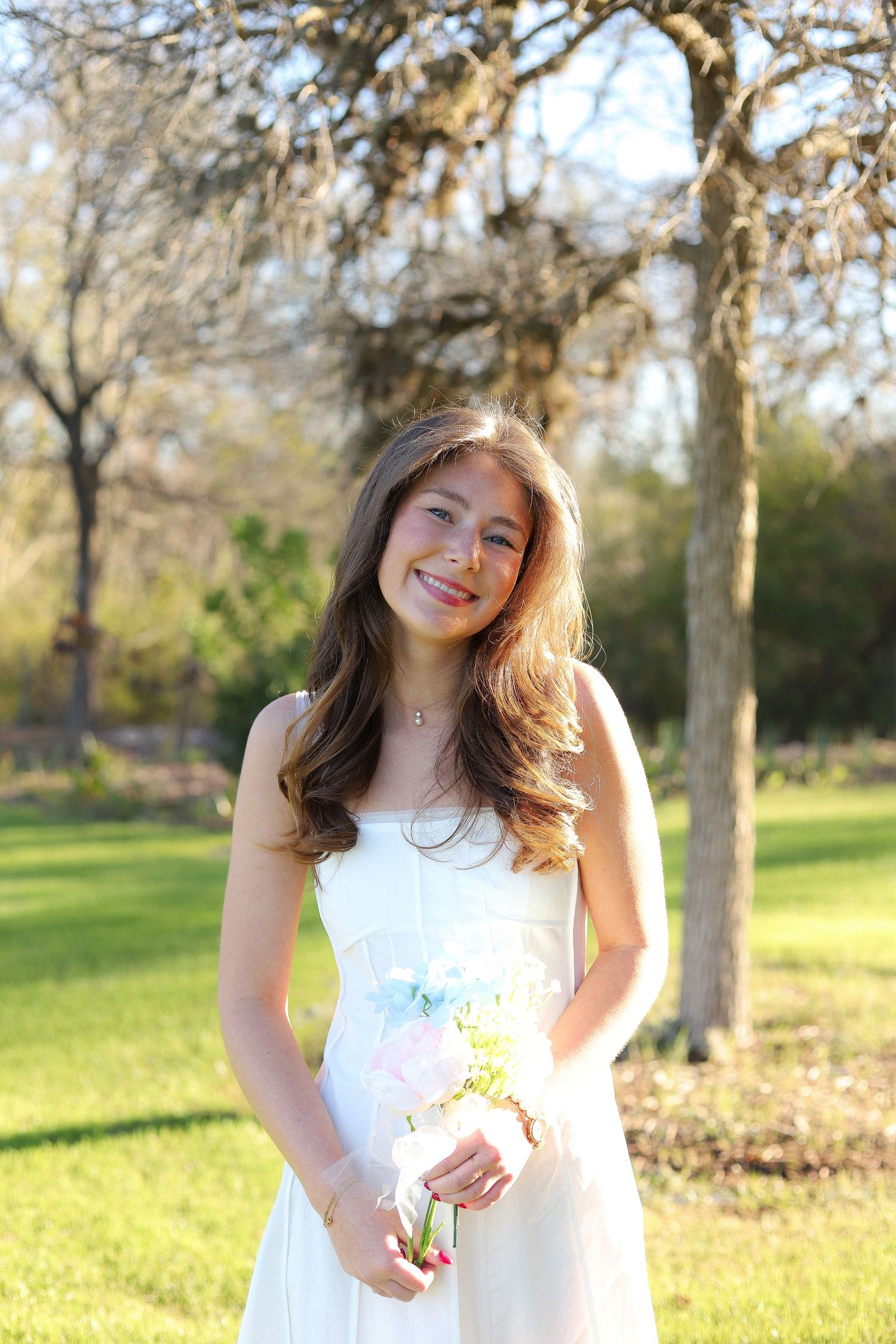 A person in a white dress poses playfully in a sunny park setting with golden afternoon light.