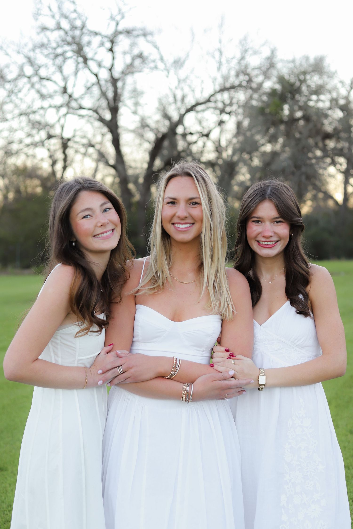 A group poses together outdoors wearing coordinated white dresses in a natural setting.