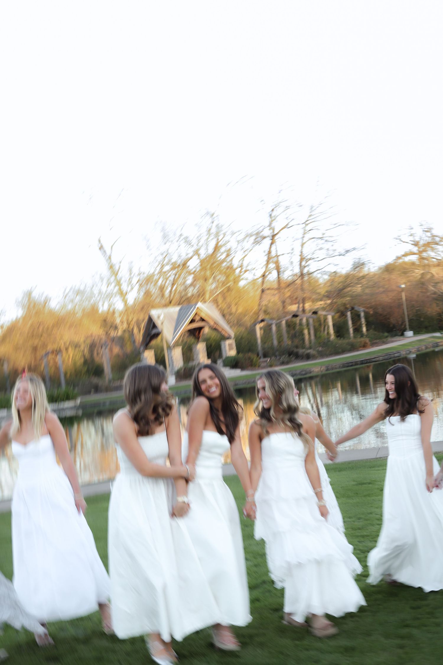 A group wearing white dresses dances and moves in a line across a grassy field at dusk.