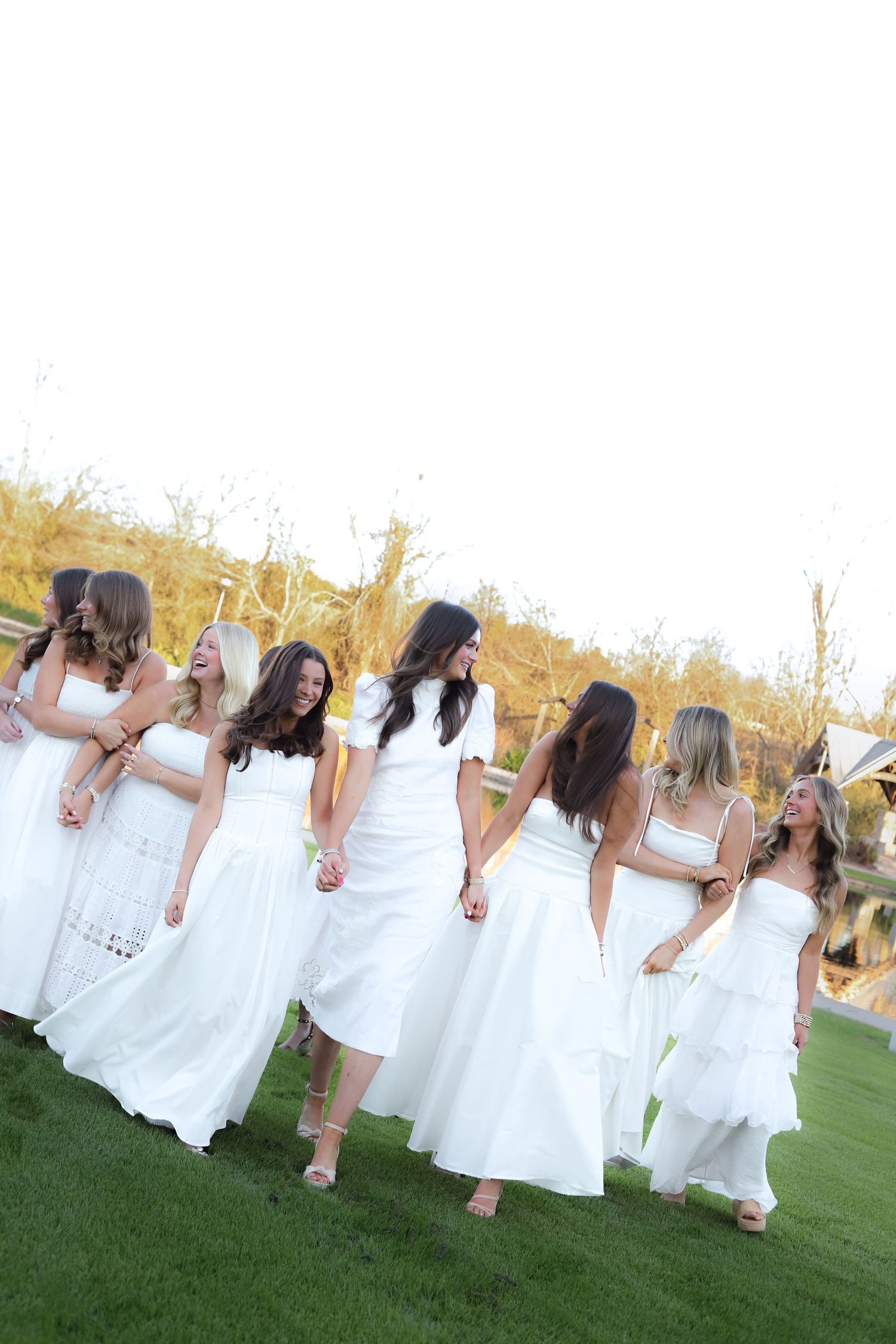 A group in white dresses walks together on grass during an outdoor event at sunset.