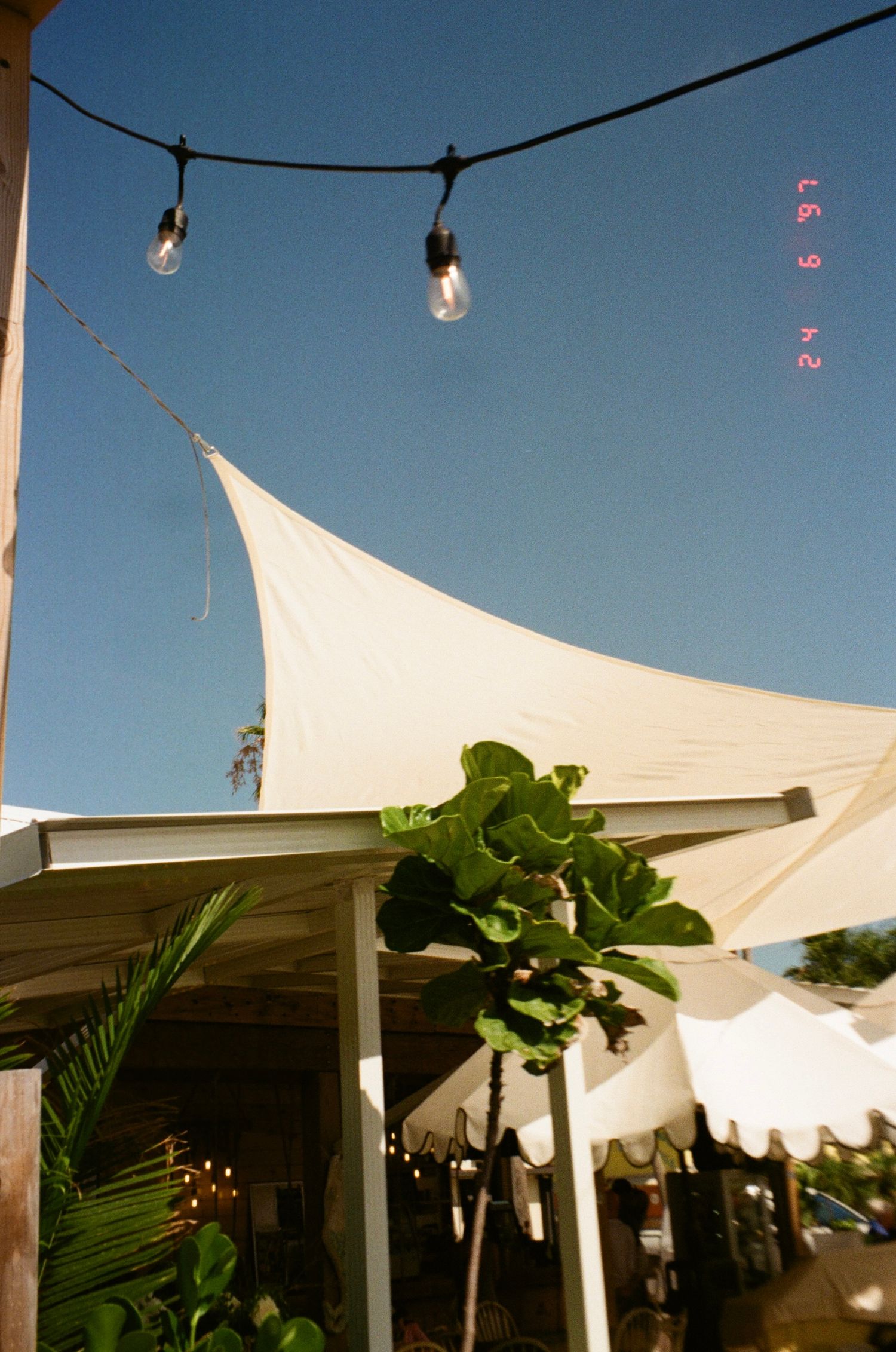 White canvas sail shades and string lights create an outdoor canopy against bright blue sky.