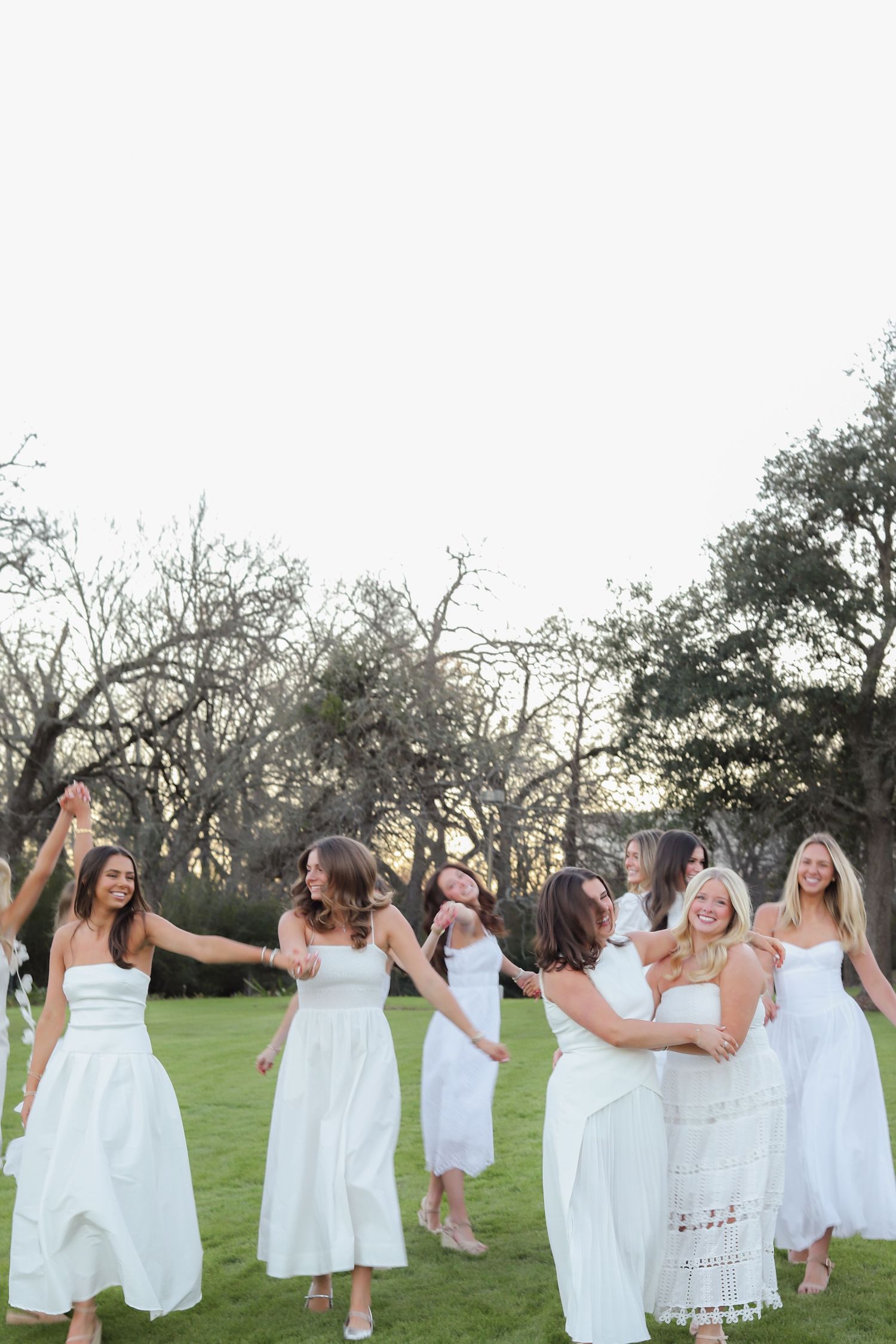 A group of people in white dresses dance and celebrate together in a grassy outdoor setting.