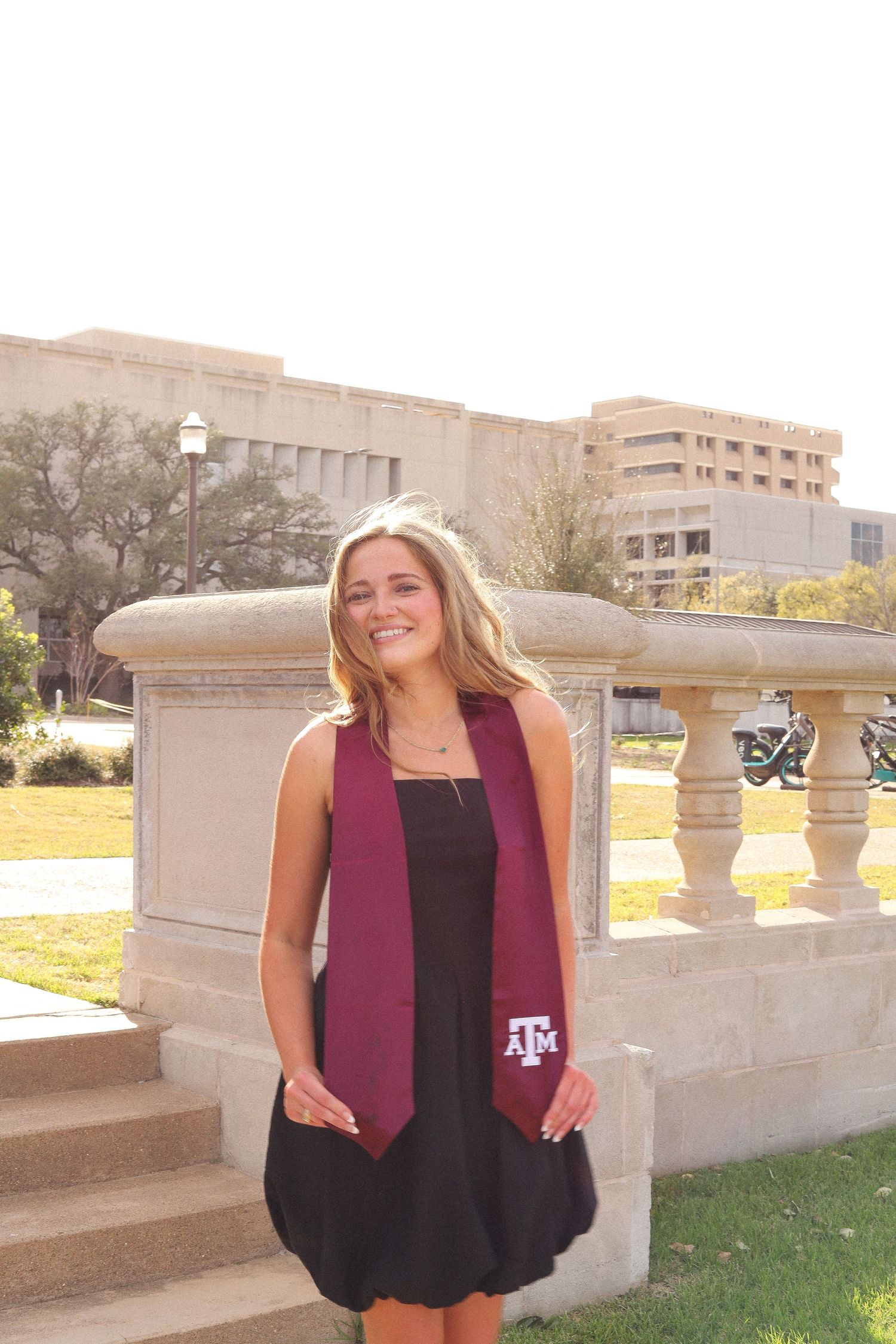 Person in black dress and maroon vest poses on stone balcony at Texas A&M campus.