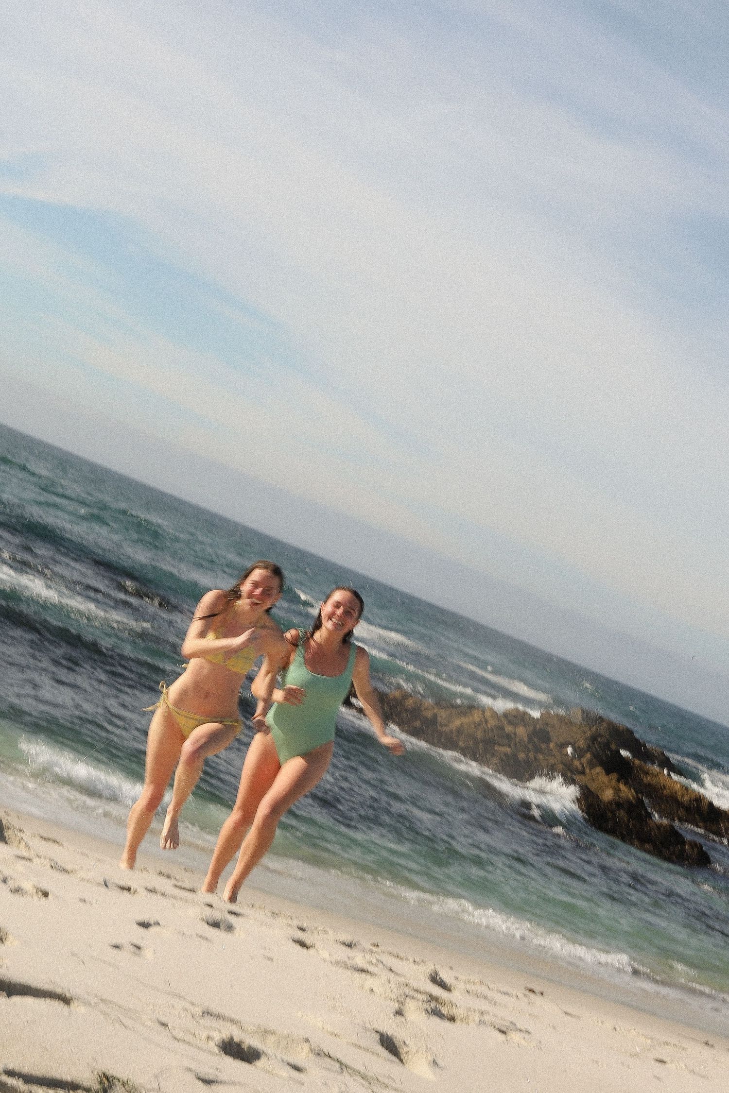 People having fun posing and playing on a sunny beach with waves crashing in the background.