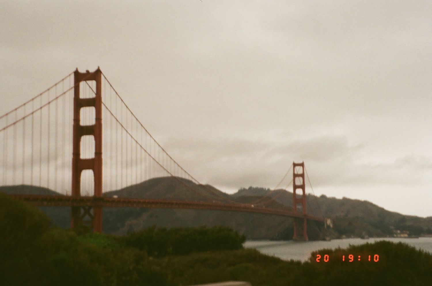 Panoramic view of the iconic Golden Gate Bridge in San Francisco on a cloudy day with mountains in the background.