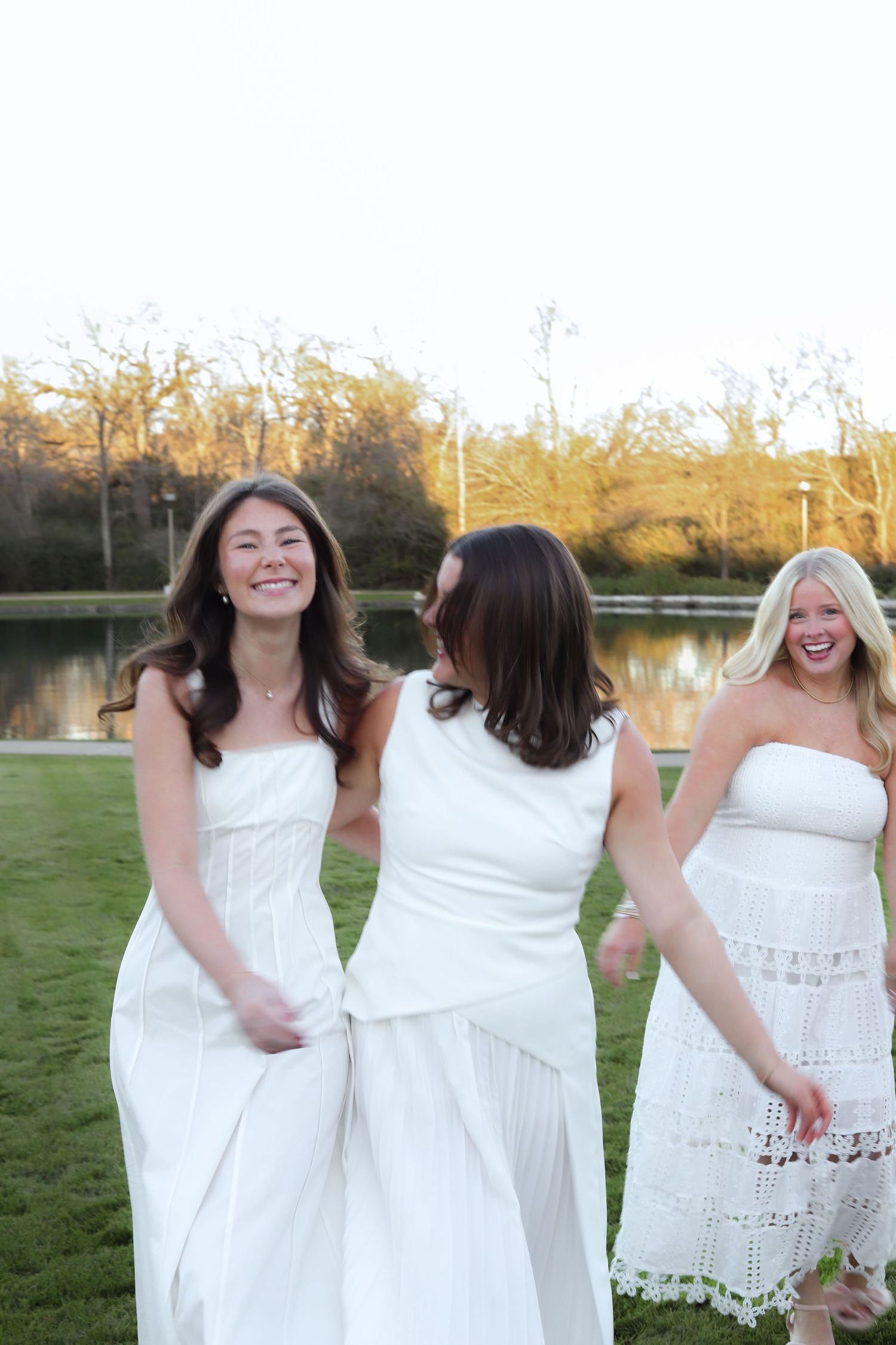 Friends in white dresses laugh and dance together in an outdoor setting.