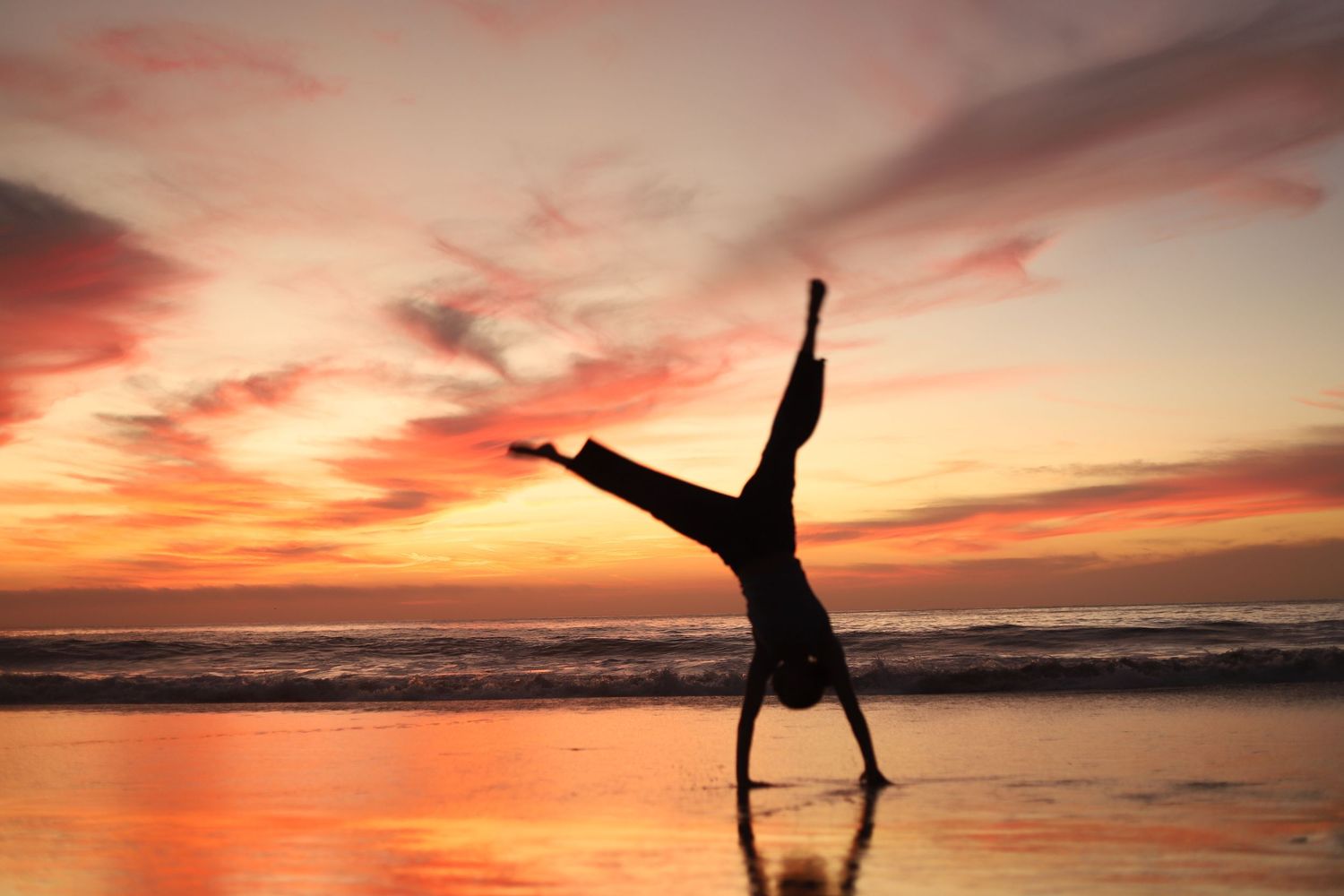 Silhouetted figures perform acrobatic poses against vibrant orange and pink sunset skies at the beach.