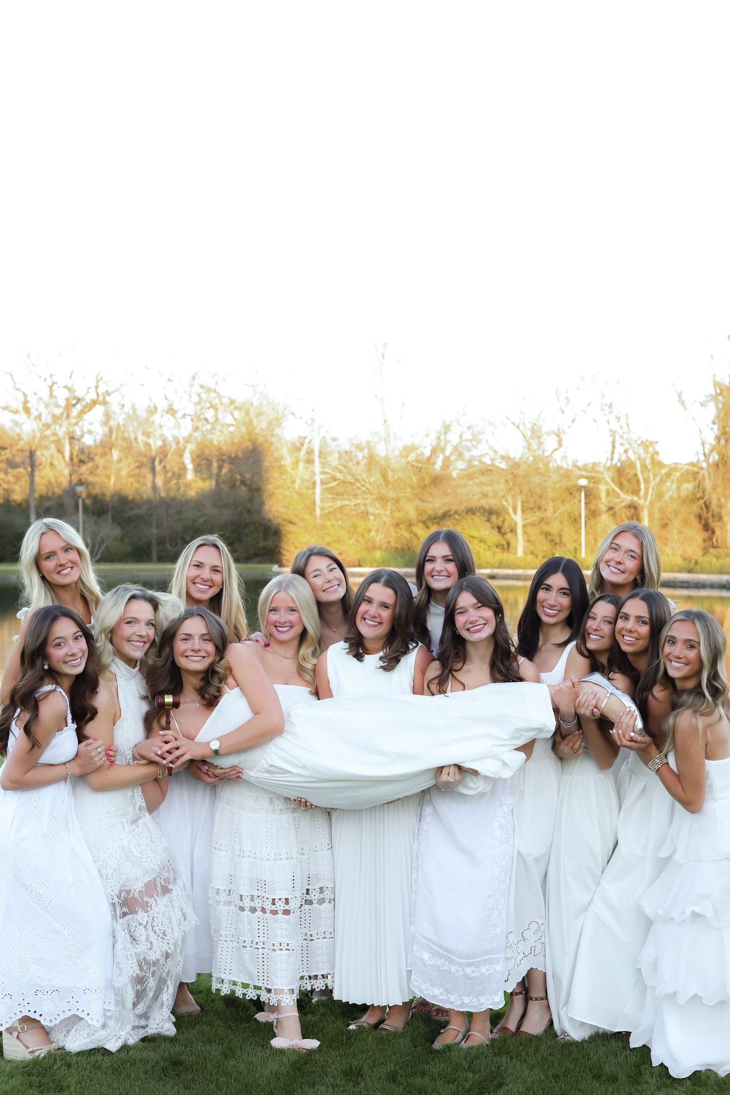 A large group of people wearing white dresses pose together outdoors in a cheerful line formation.