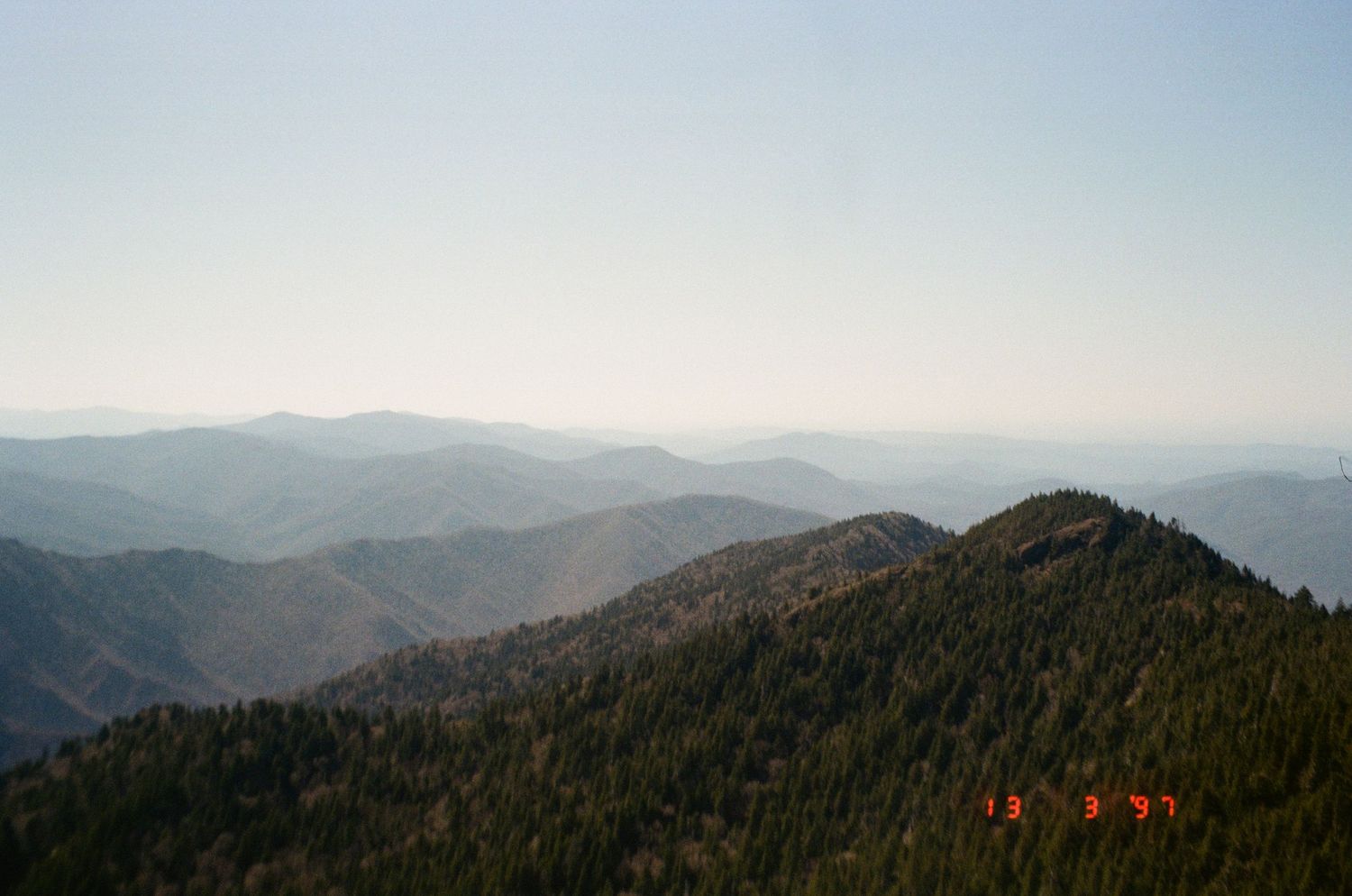 Panoramic view of rolling mountain ranges covered in dense forest stretching to the misty horizon.