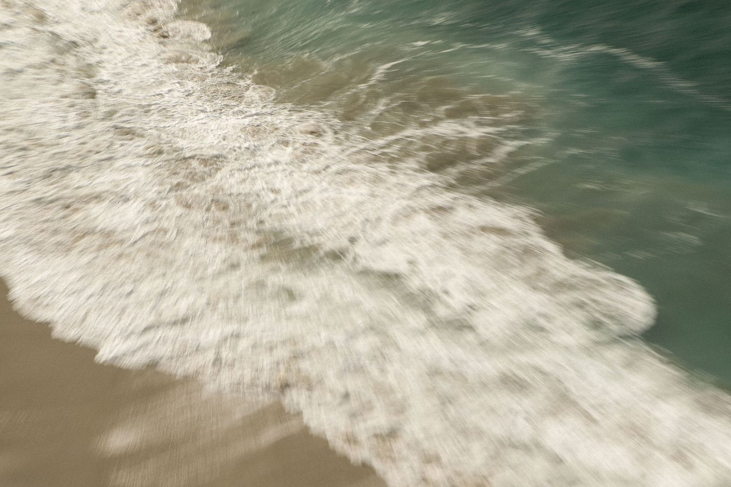 Ocean waves rolling onto sandy beach with soft focus creating dreamy effect.