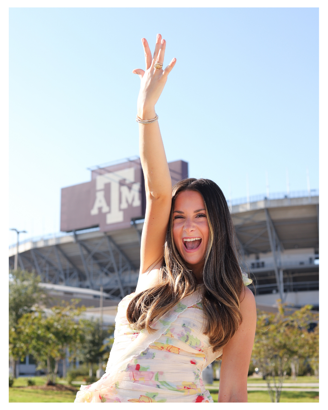 Person in floral dress poses cheerfully outside Kyle Field stadium.