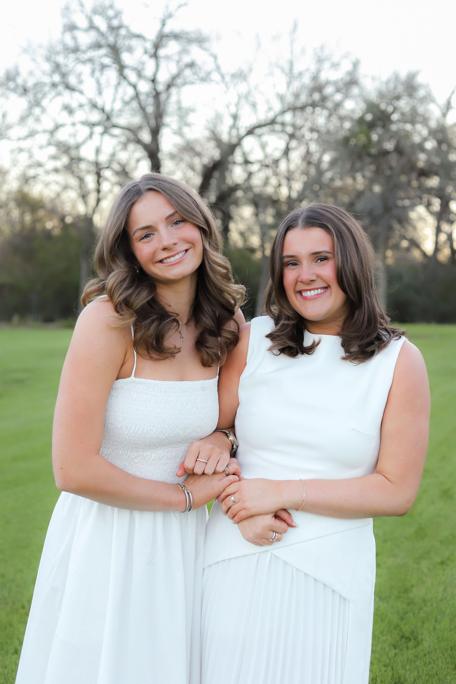 Two people in white dresses embrace while posing in a grassy field.
