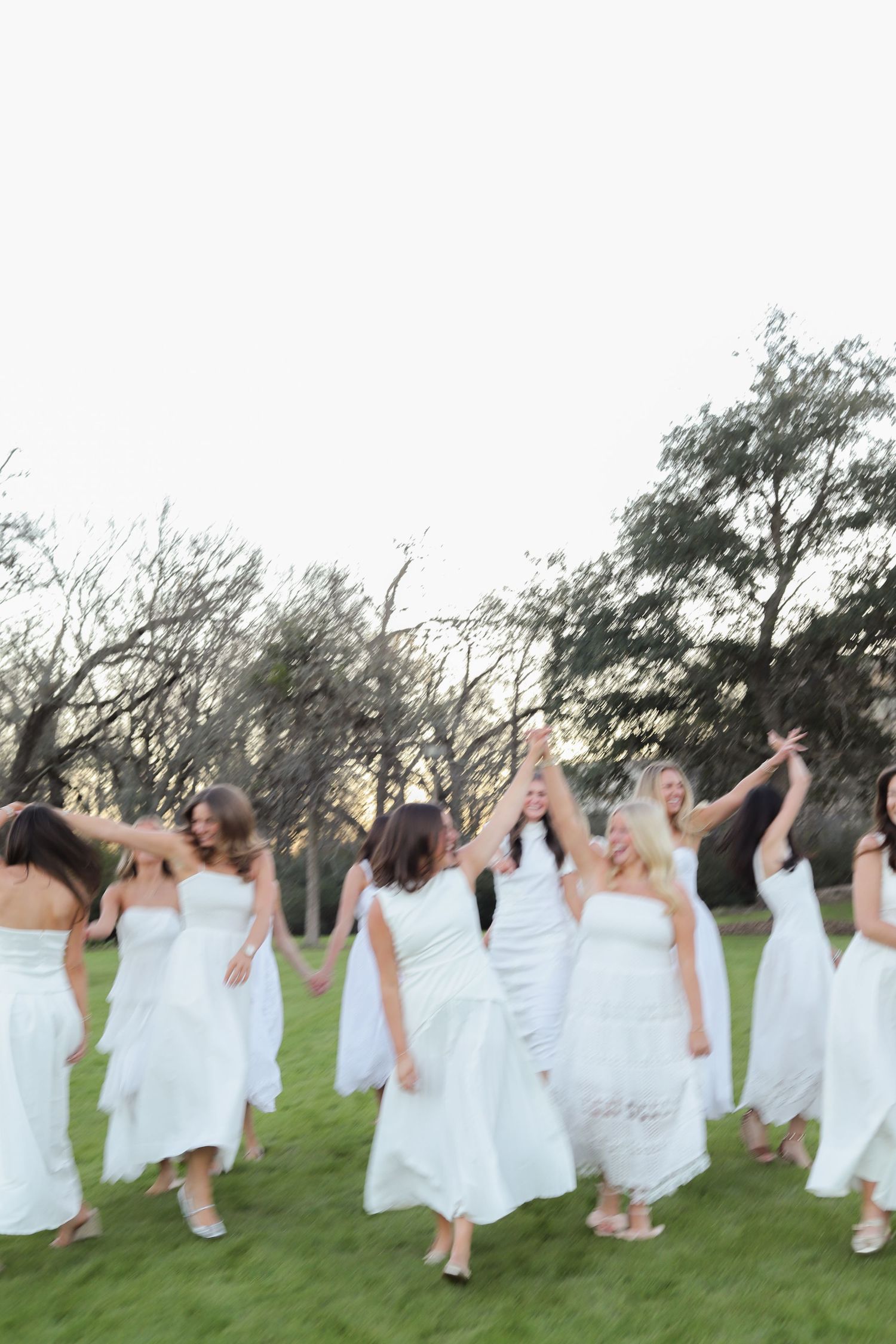 A group in white dresses dance and celebrate together in a field during sunset.