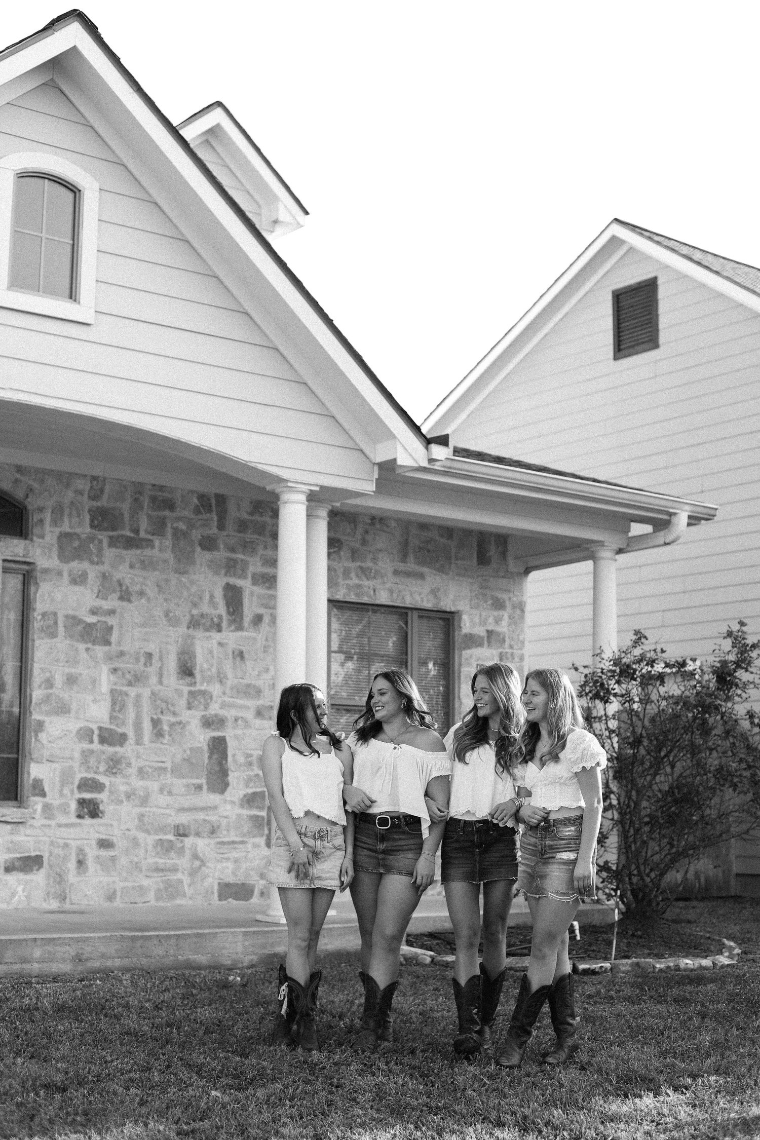 Black and white photo series of friends posing casually in front of a stone and white house.