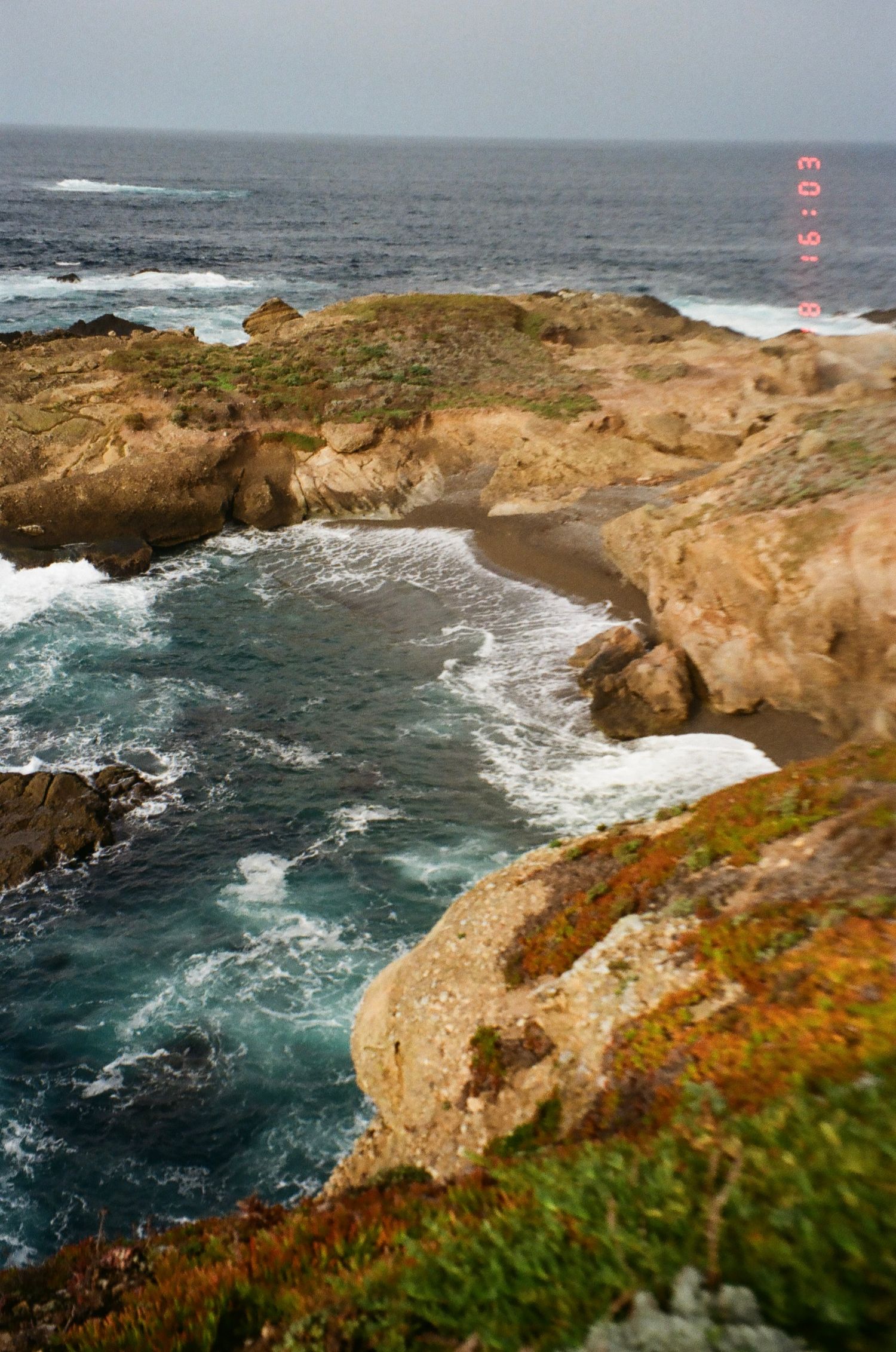 Dramatic rocky coastline with crashing waves against rugged cliffs and blue ocean waters on a sunny day.