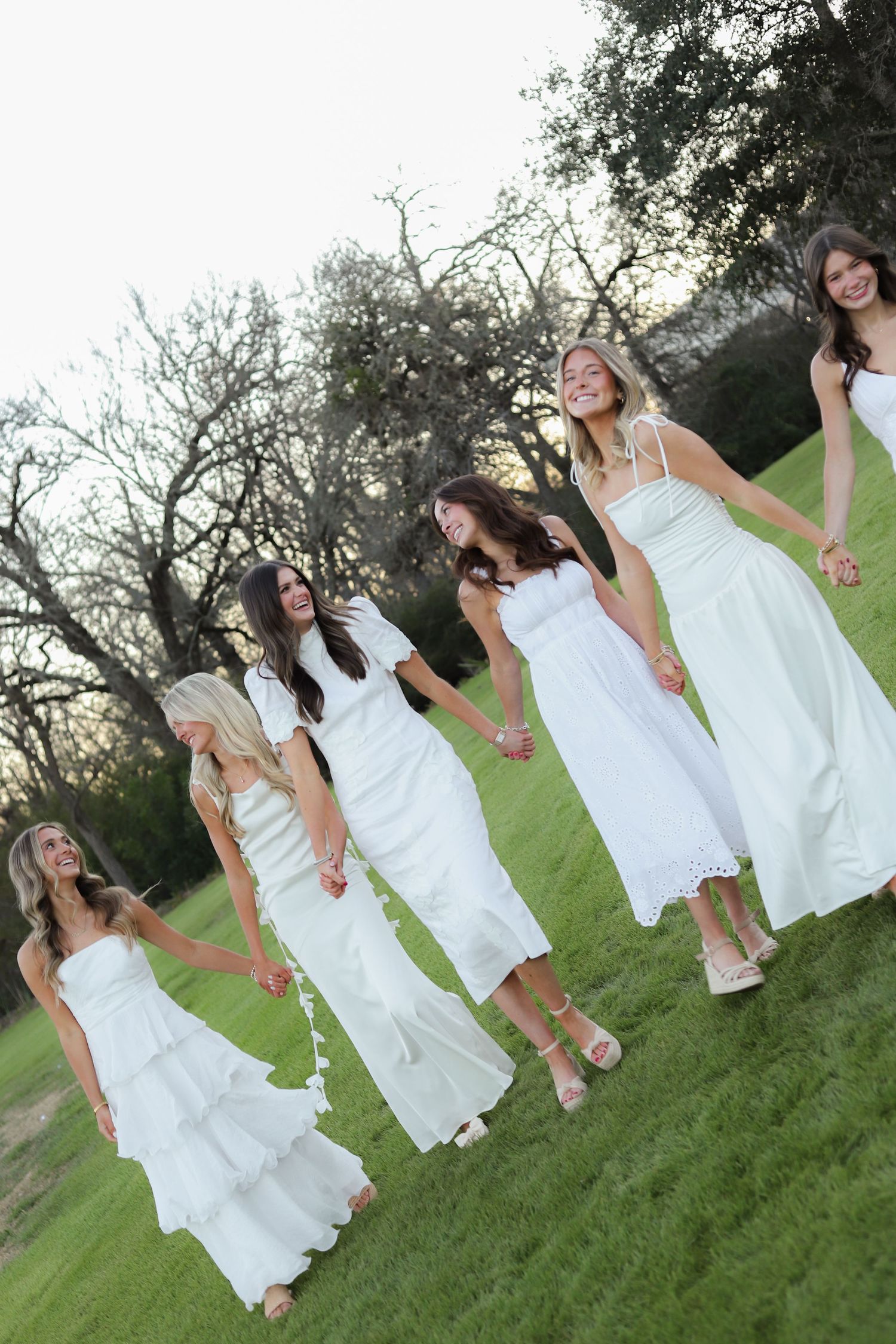 A group in flowing white dresses stands together on a grassy hill during golden hour.