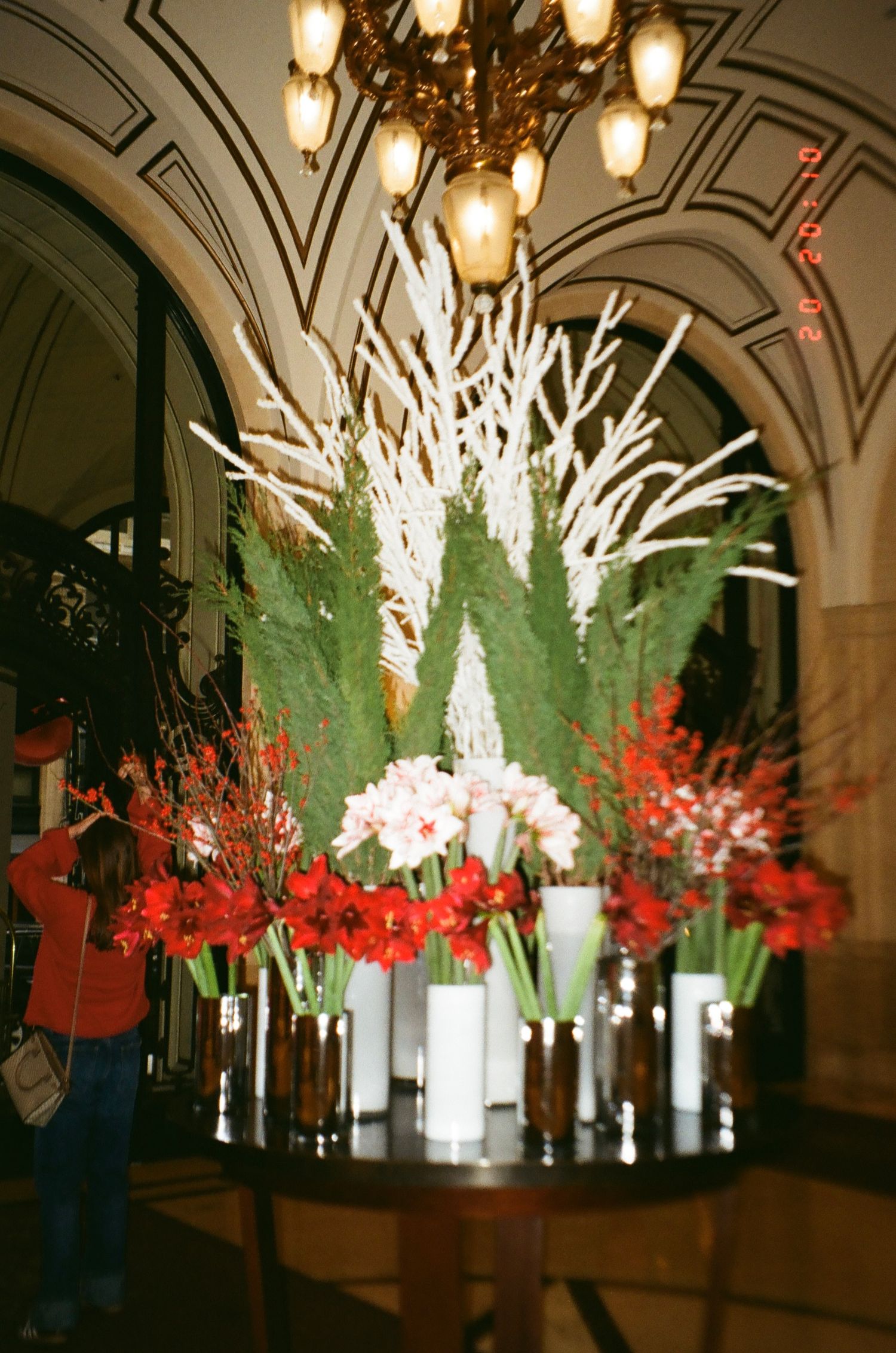 Elegant event space decorated with illuminated white branches and red floral arrangements under arched ceilings.