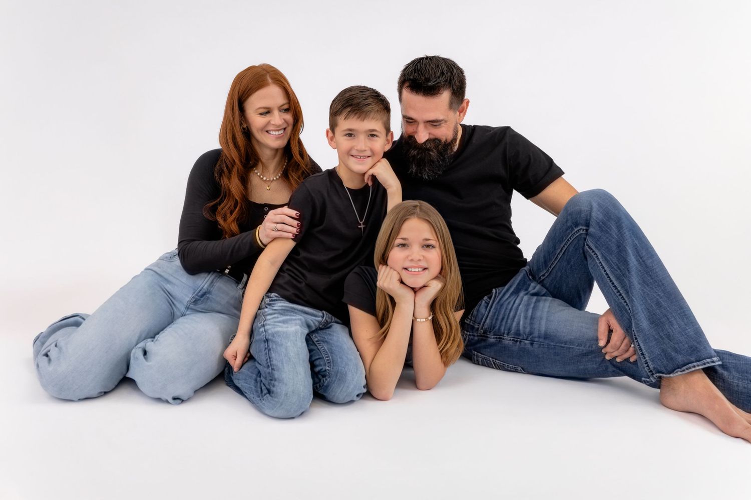 A family in casual denim outfits lies together on a white background in a playful photo series at a family session in Murfreesboro, TN.