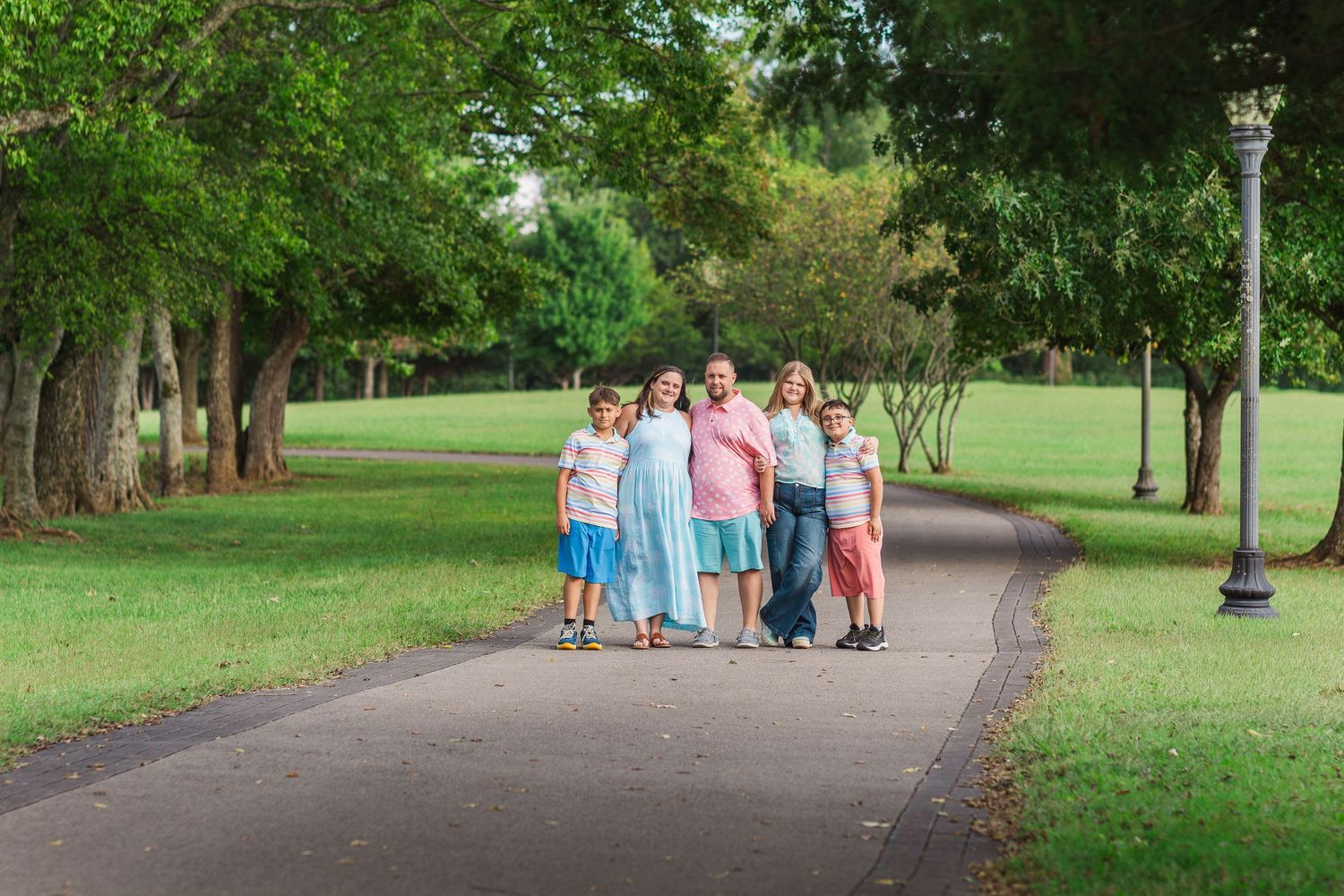Family wearing coordinated outfits in soft colors walking together during an outdoor photography session in a park