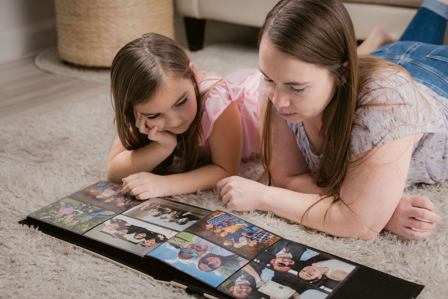 Mother and daughter lying on carpet together looking at a family photo album at home in Murfreesboro, Tennessee.