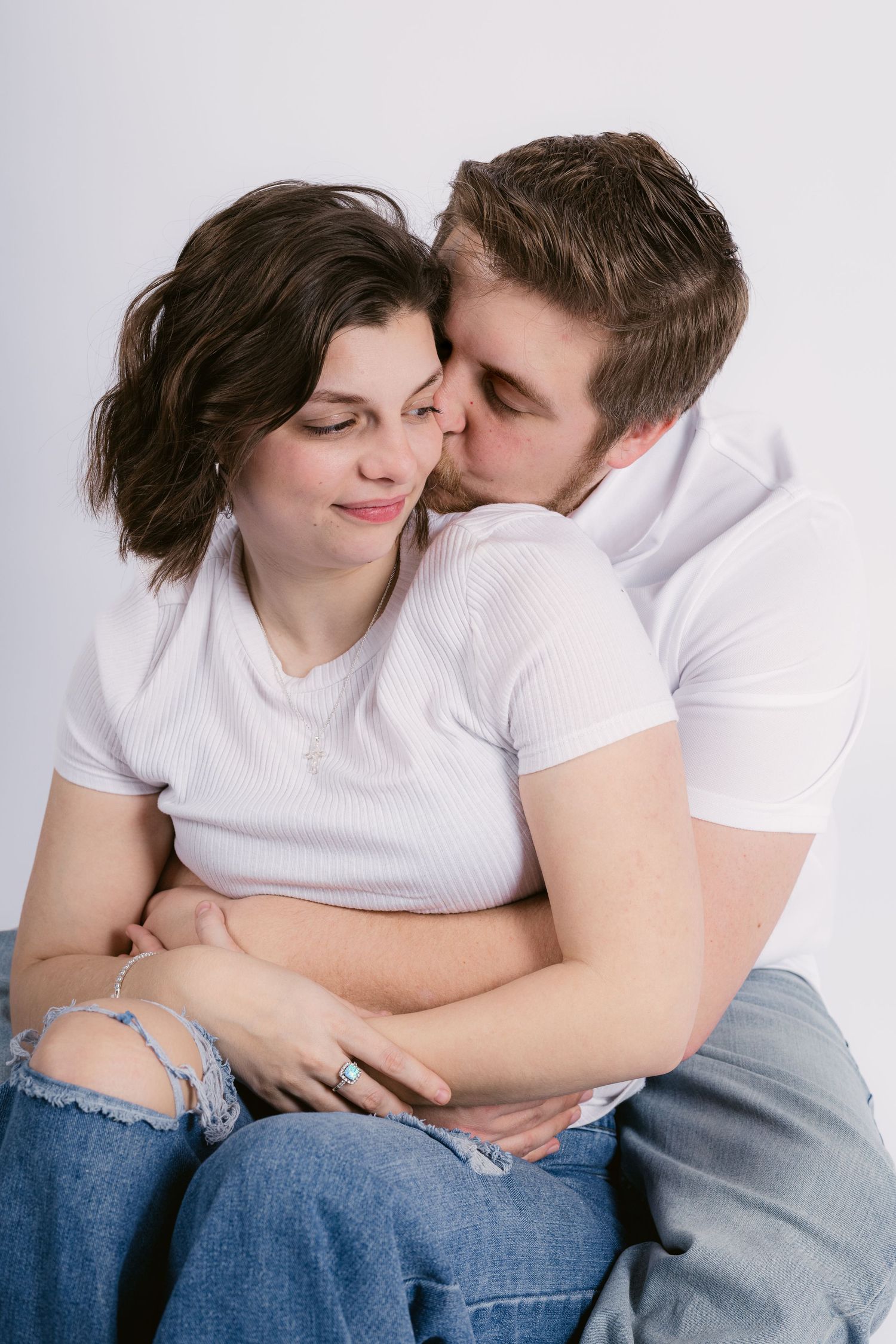 A young couple in white t-shirts and jeans share a tender moment, with the man kissing the woman's cheek in Murfreesboro, Tennessee.