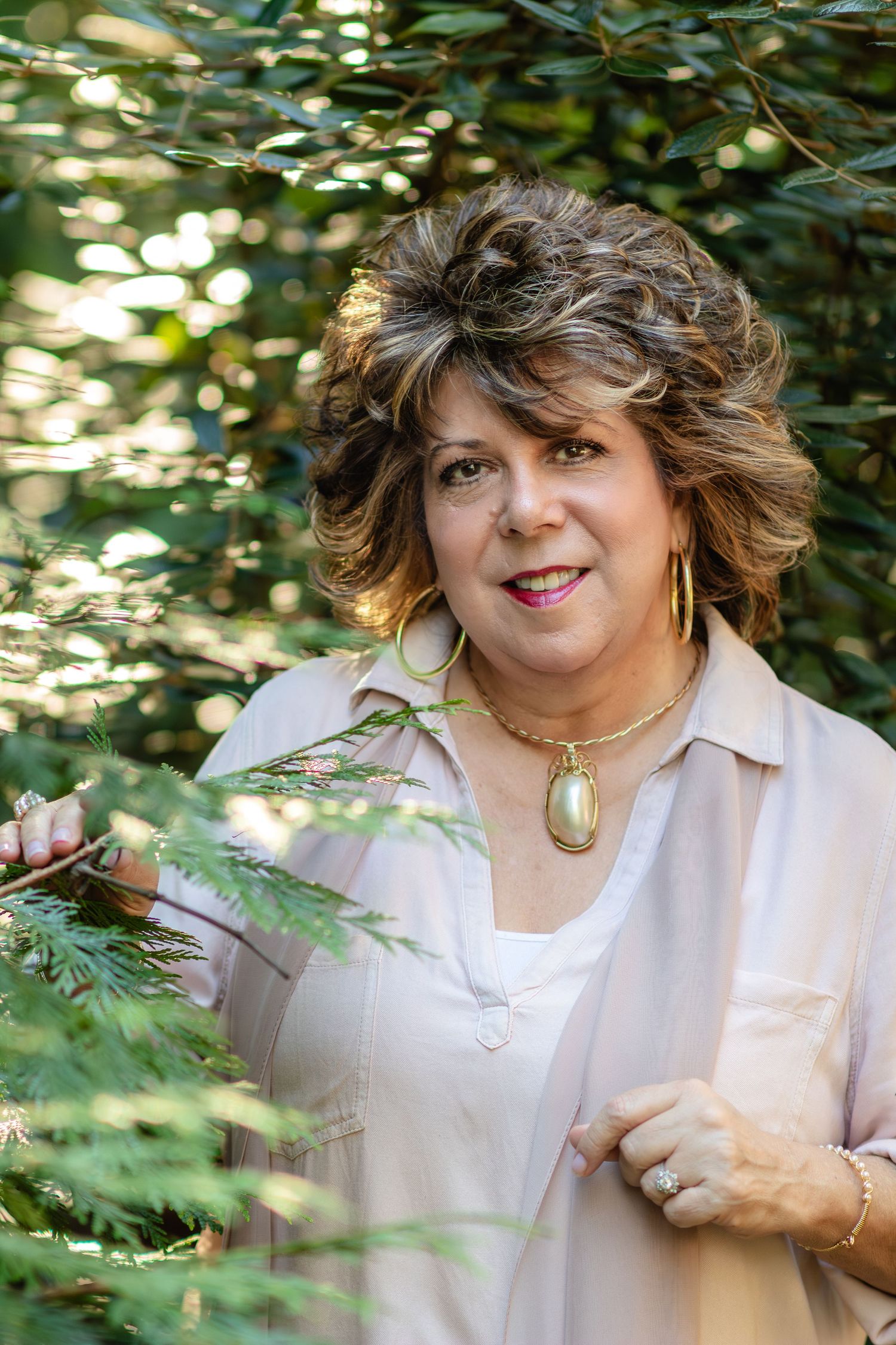 Woman wearing a soft neutral blouse photographed outdoors with natural light and greenery for a portrait session