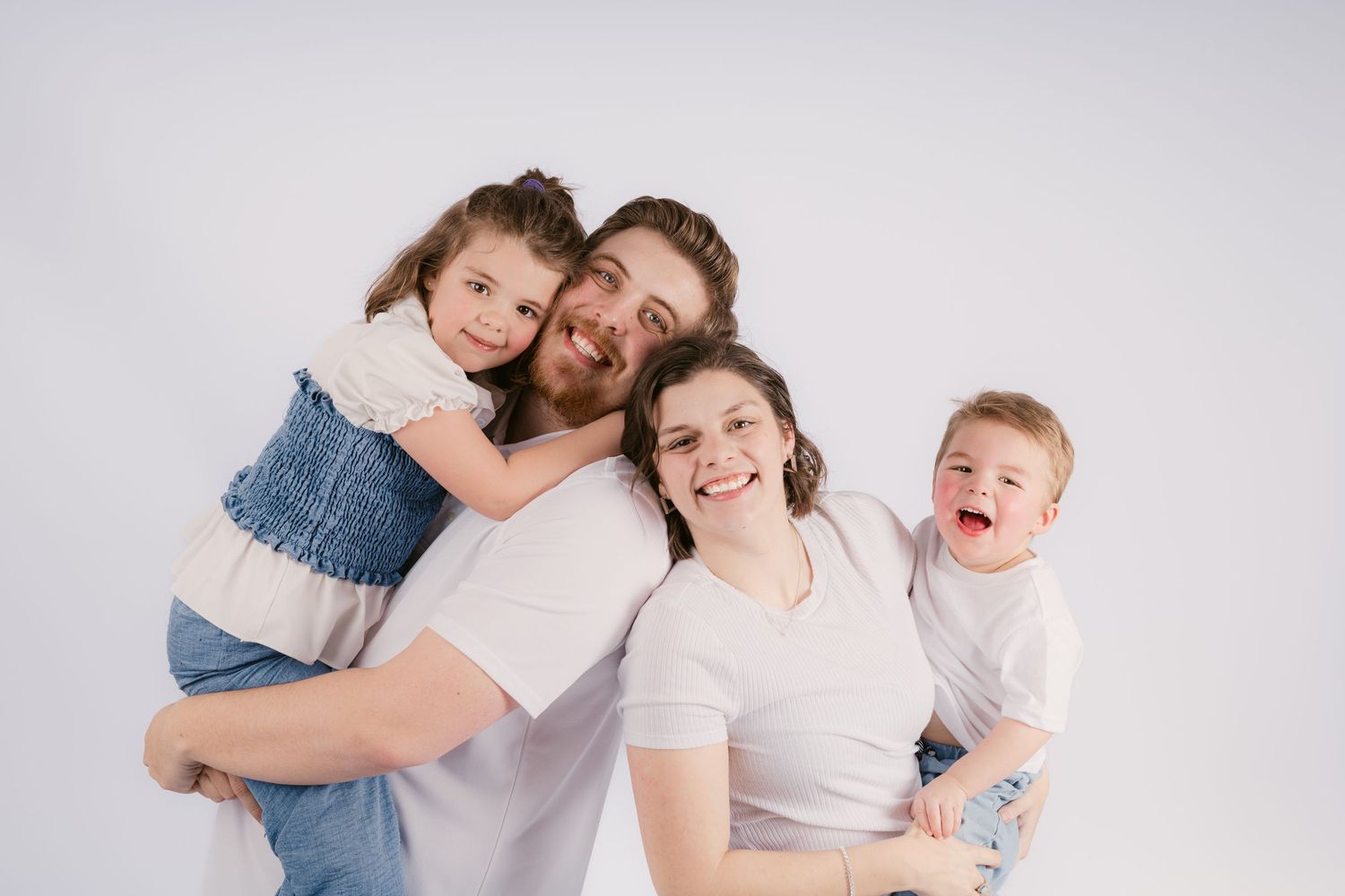 Happy family of four posing together, parents holding two young children, smiling against a white background in Rutherford County.