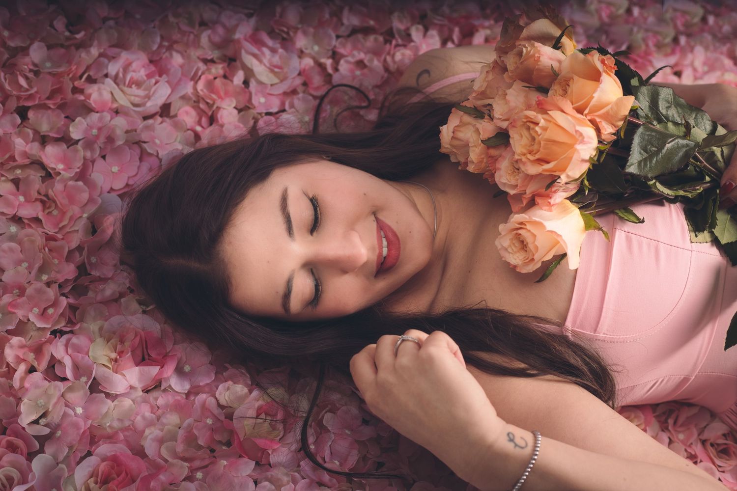A woman lying in pink flowers holding roses during a creative portrait session in Murfreesboro, Tennessee