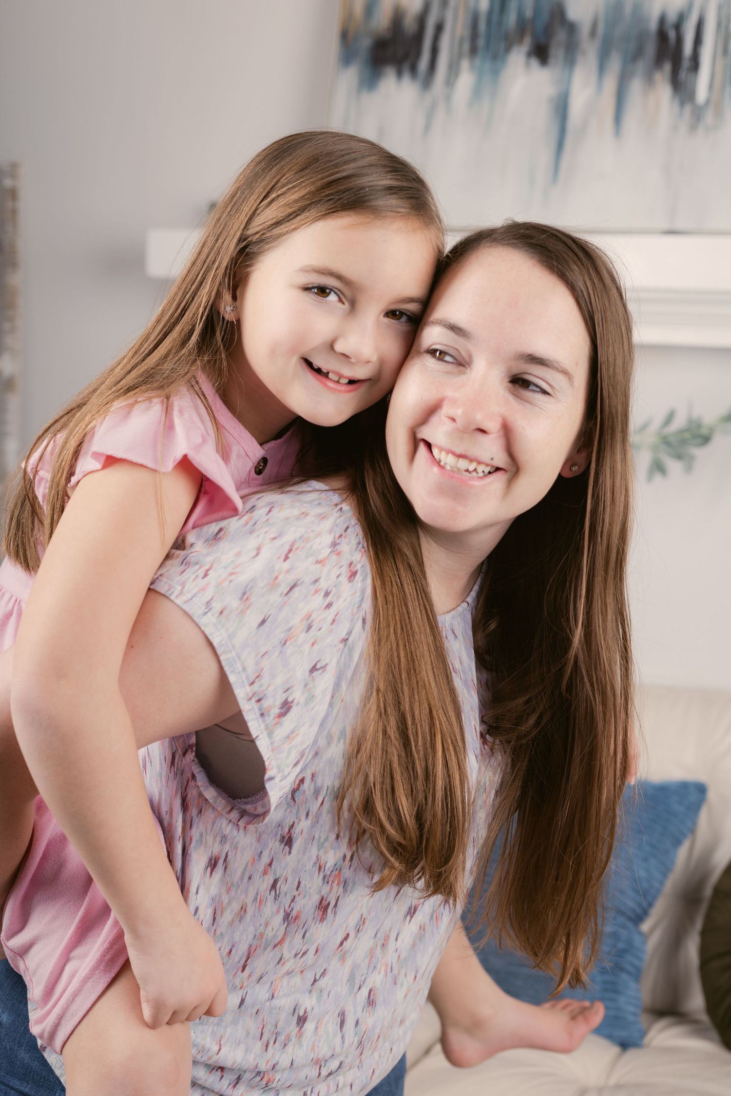 A smiling mother and young daughter share a joyful piggyback moment together indoors in Rutherford County.