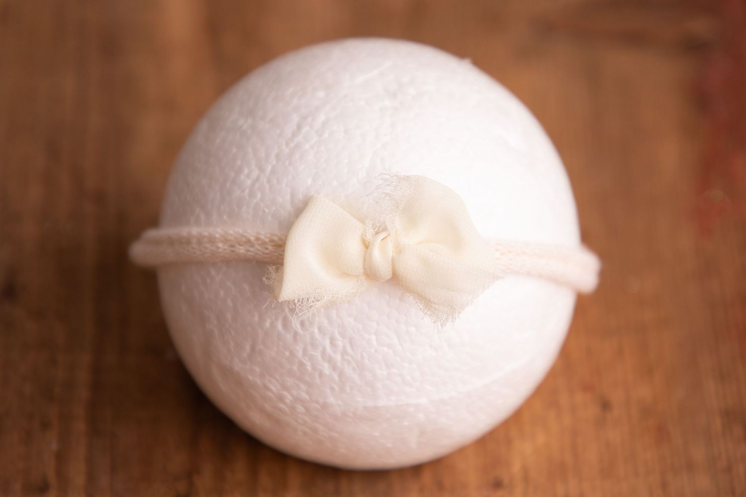 White knit ball with a small ivory satin bow headband on a wooden background.