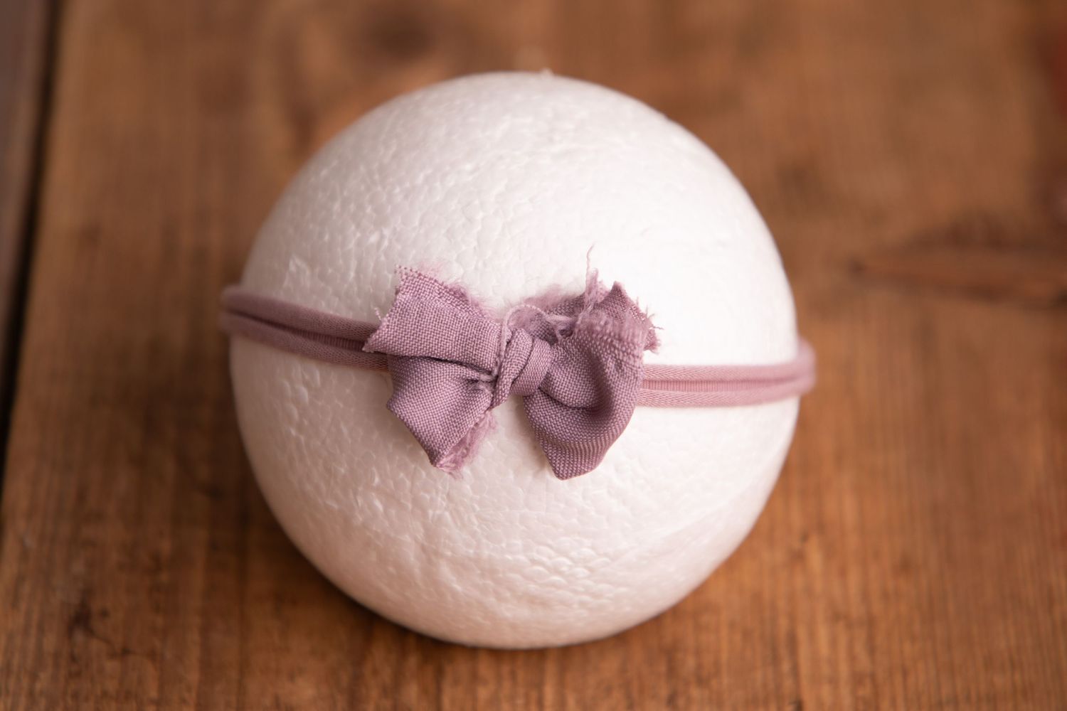 White wool felt ball with dusty pink fabric bow headband on wooden background.