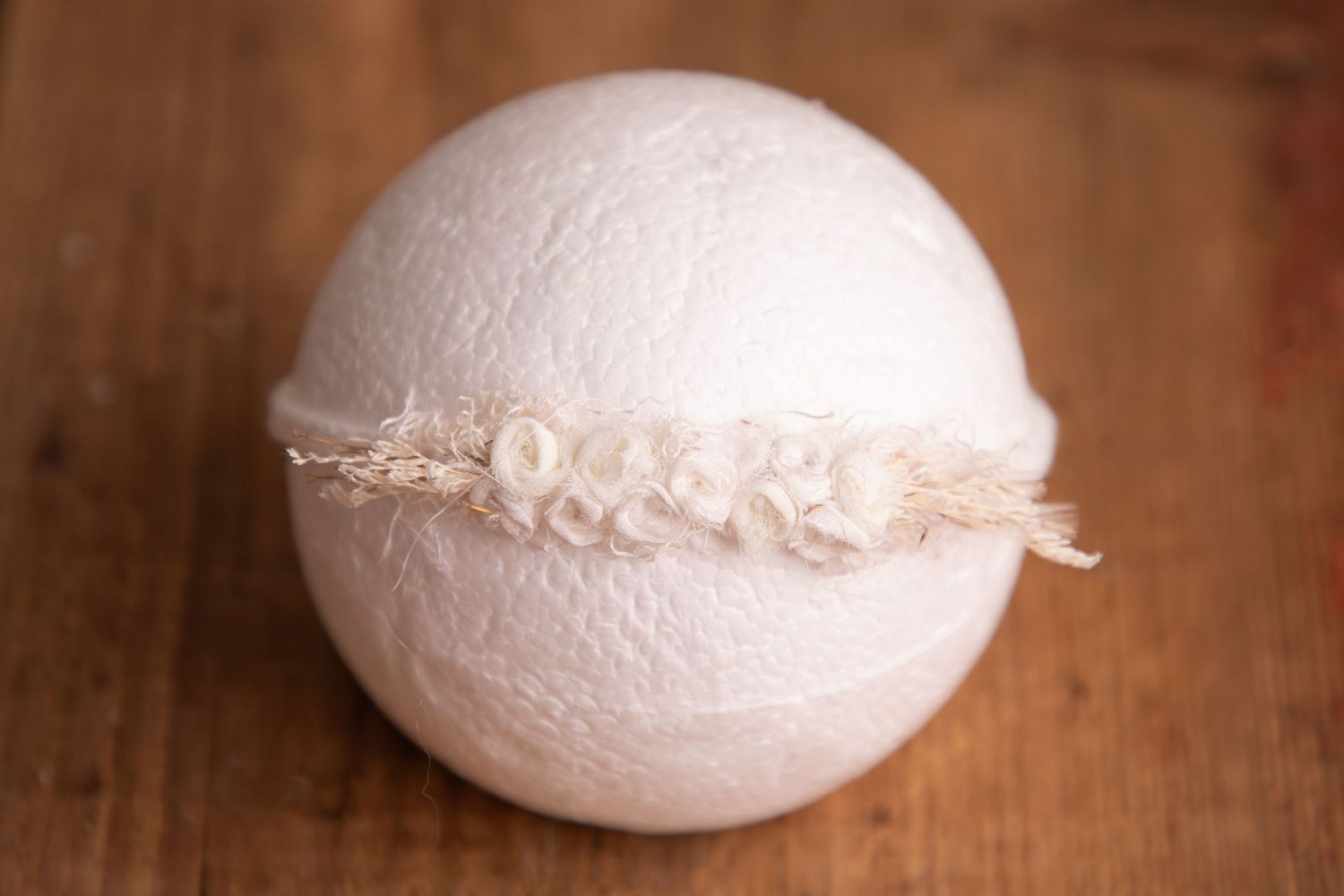 Ivory floral lace headband displayed on white ball newborn photography prop on wood surface.