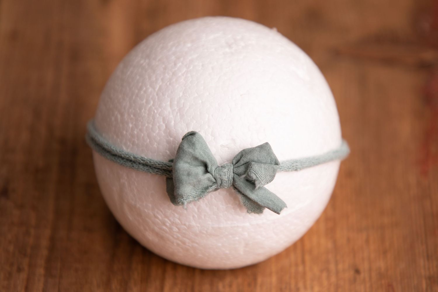 White wool felt ball with sage green fabric bow headband on wooden background.