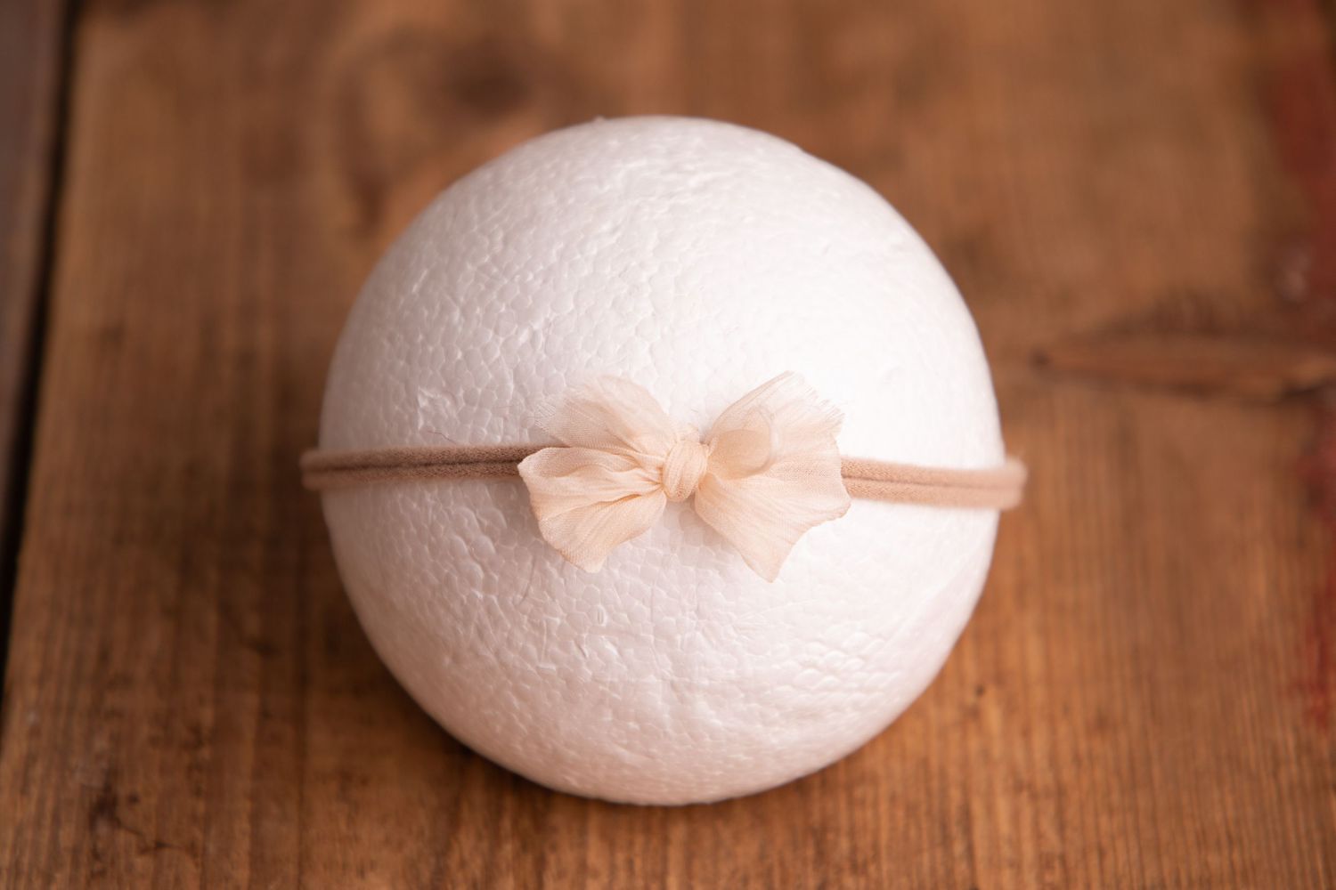 White fluffy newborn photography prop ball with a delicate cream bow headband on wood surface.