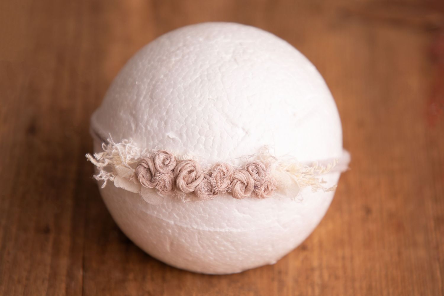 Blush pink rosette lace headband on white ball newborn photography prop on wooden backdrop.