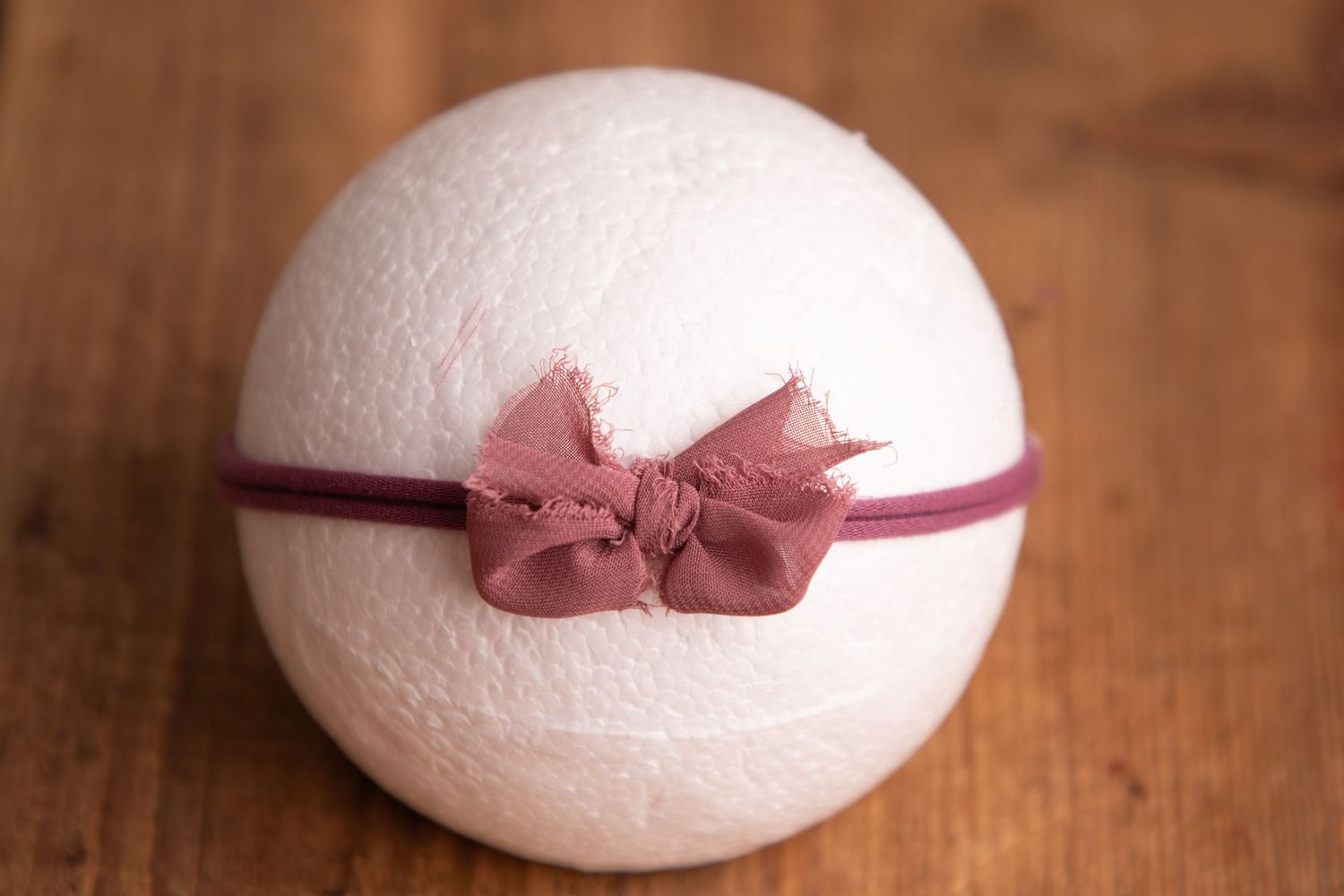 White wool felt ball with mauve pink fabric bow on burgundy elastic headband.